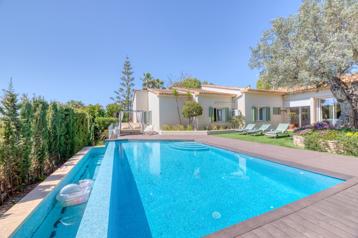 Exterior view of a Mediterranean villa with a rectangular swimming pool, wooden decking, and landscaped gardens in Santa Ponsa.