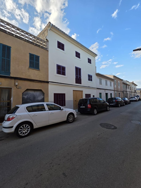 Exterior view of a multi-story townhouse in Campos featuring a white rendered facade, wooden shutters, and street parking.