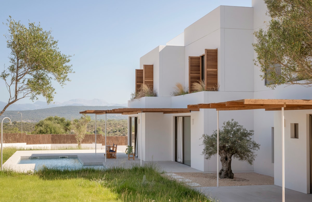 Modern white house featuring wooden shutters and a swimming pool with views of the distant mountains and green landscape.