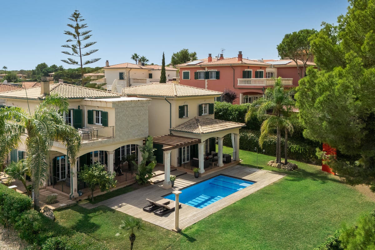 A two-story villa with Mediterranean architecture, a tiled roof, green louvered shutters, and a swimming pool in the garden.