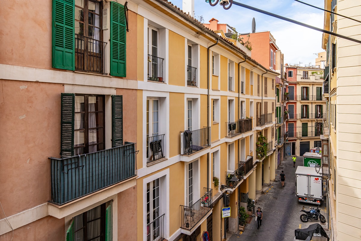 Exterior view of a traditional Mediterranean apartment building facade with mustard-yellow walls and green wooden shutters.