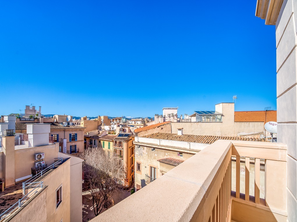 An elevated view from a rooftop terrace looking out over the densely packed stone buildings and terracotta roofs of an Old Town.