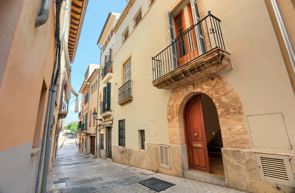 Exterior view of a multi-story townhouse in a narrow cobblestone street, featuring a stone arched entrance and iron balcony.