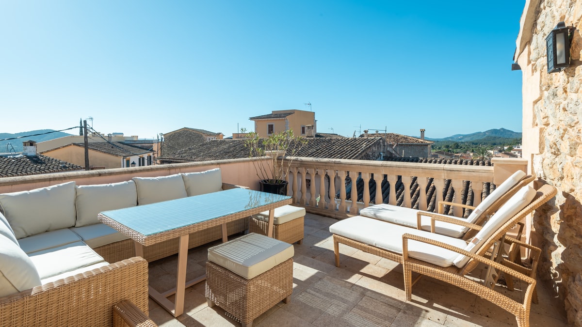 Outdoor seating and sun loungers on a rooftop terrace overlooking village rooftops and hills