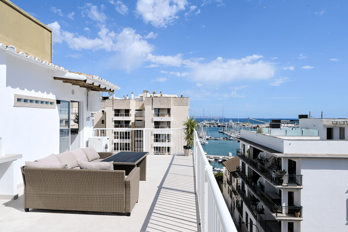 A sunny rooftop terrace overlooking the Santa Catalina marina with woven lounge furniture and a white railing.