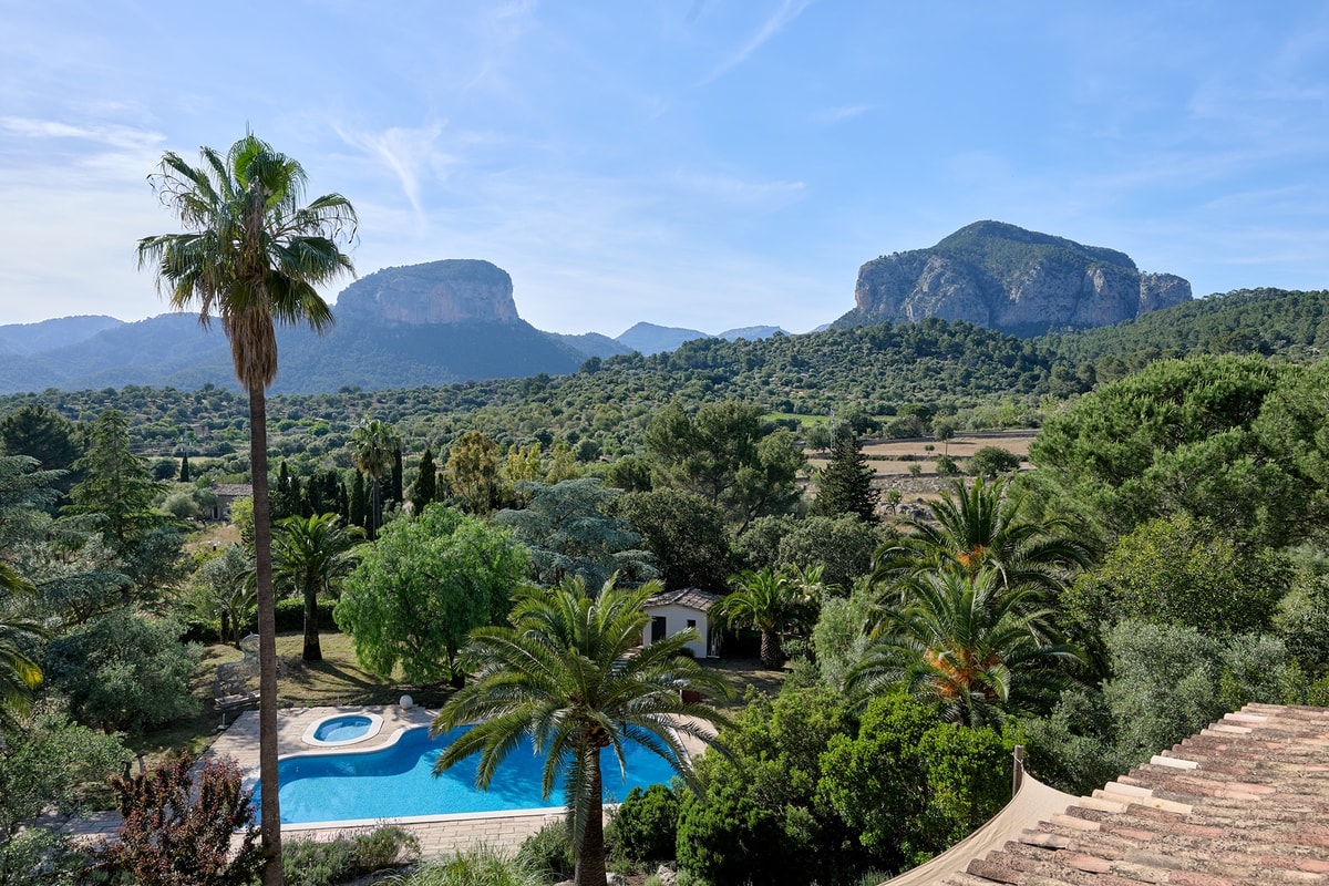 Wide shot of a Mallorca finca estate featuring a swimming pool, palm trees, and the Tramuntana mountain range in the distance.