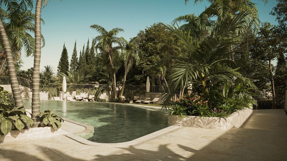 Outdoor swimming pool surrounded by palm trees and lush vegetation with stone paved terrace area under natural daylight.