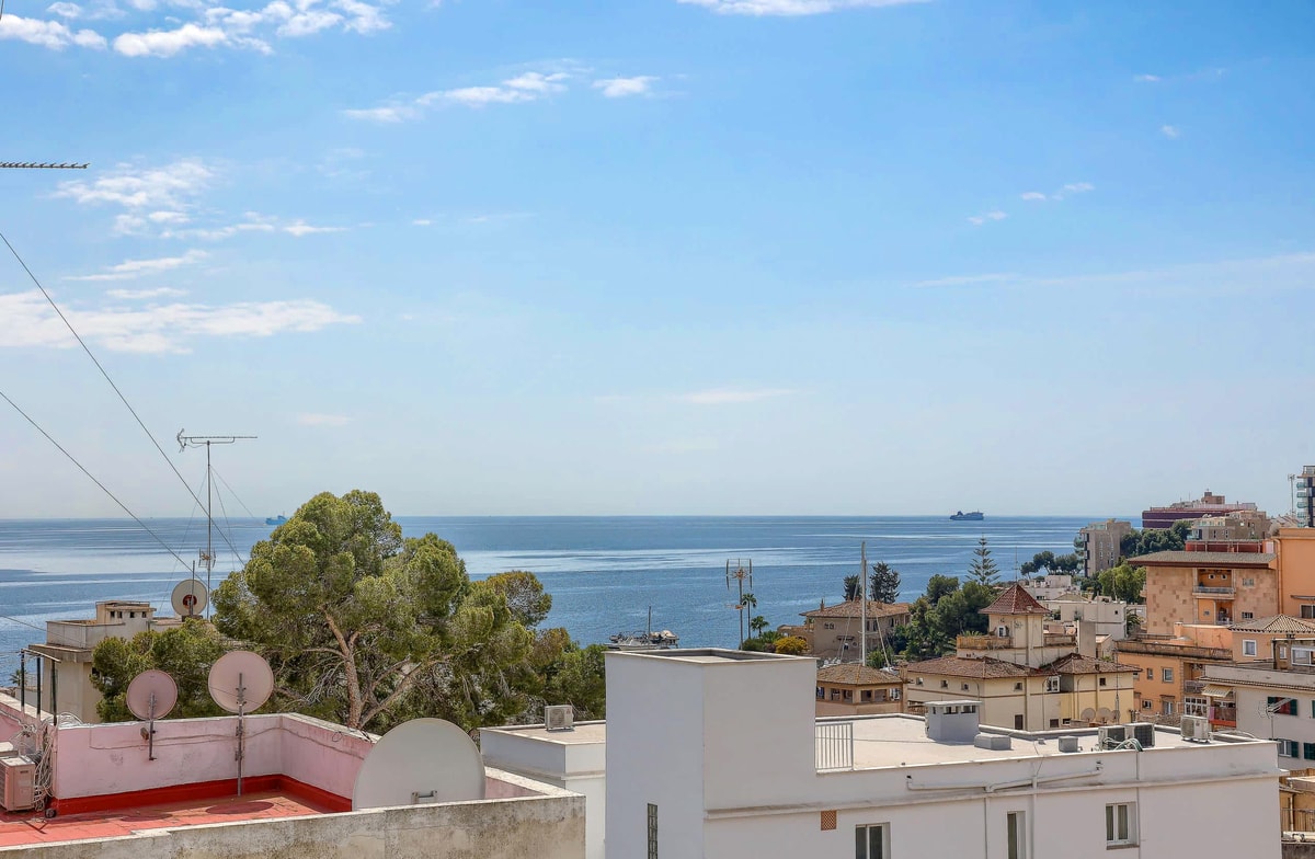 Elevated view overlooking the San Agustin coastline and Mediterranean sea under a clear blue sky with urban rooftops below.