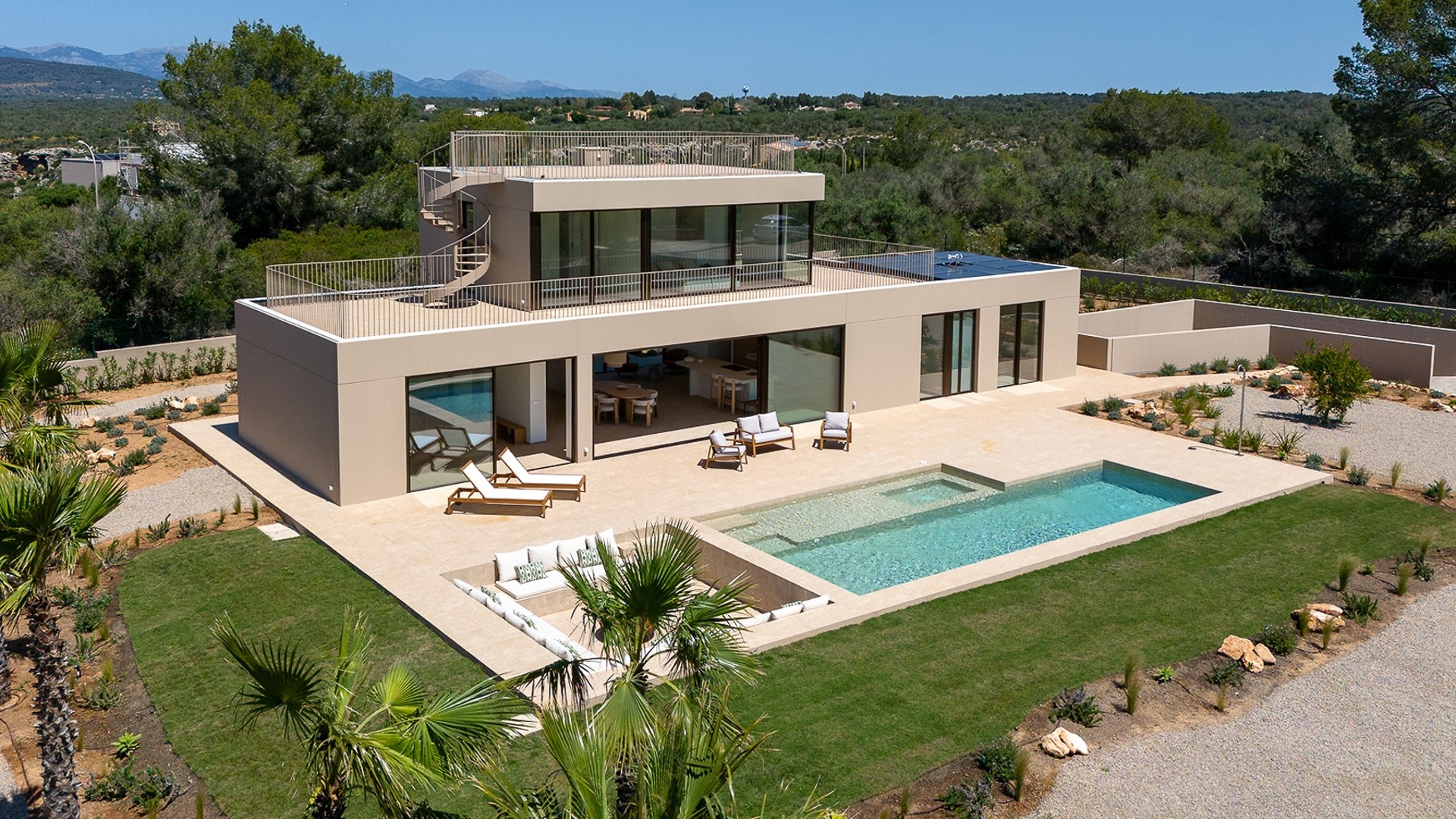 Aerial view of a modern beige villa in Son Gual featuring a rectangular swimming pool, terrace, and mountain backdrop.