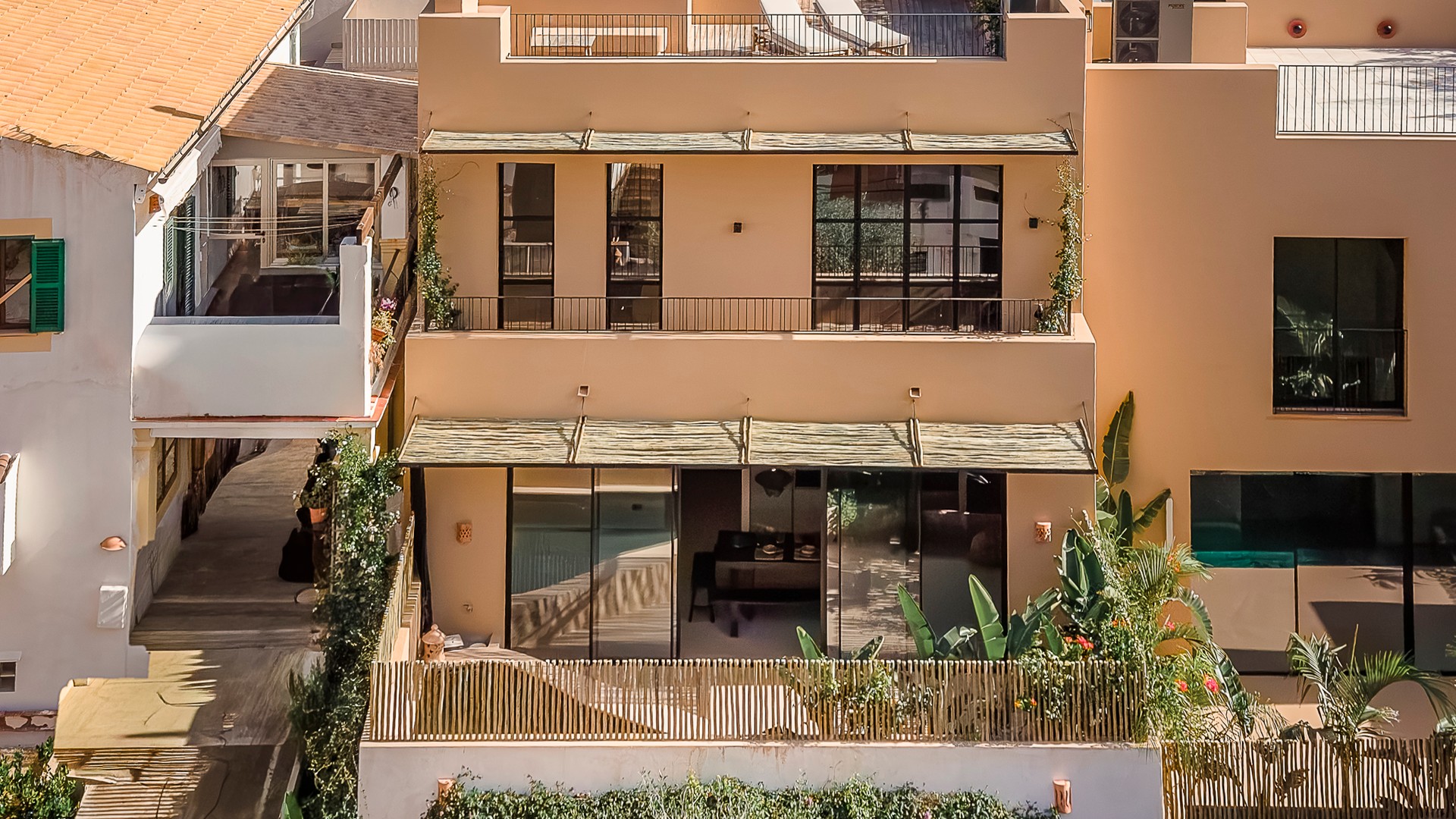 Exterior view of a multi-level townhouse in Genova featuring a beige stucco facade, large glass sliding doors, and a rooftop terrace.
