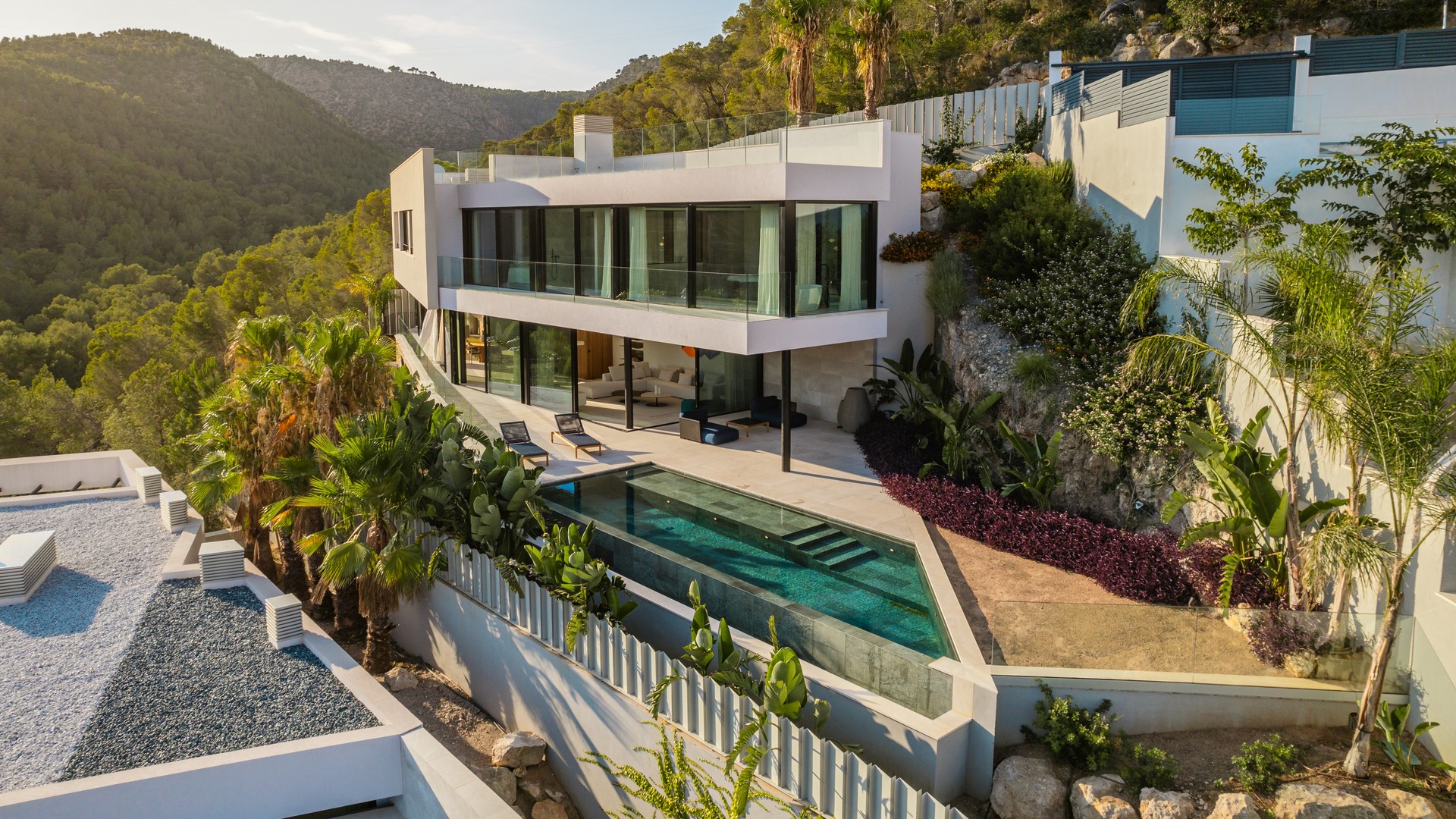 A contemporary white villa built into a hillside with floor-to-ceiling glass walls, a tiered terrace, and a private pool.