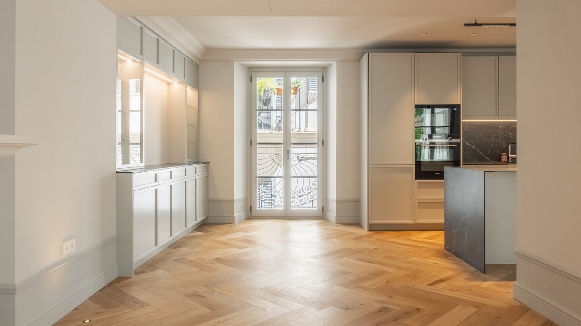 Interior view of a renovated apartment featuring light oak herringbone flooring, contemporary kitchen cabinetry, and French doors.