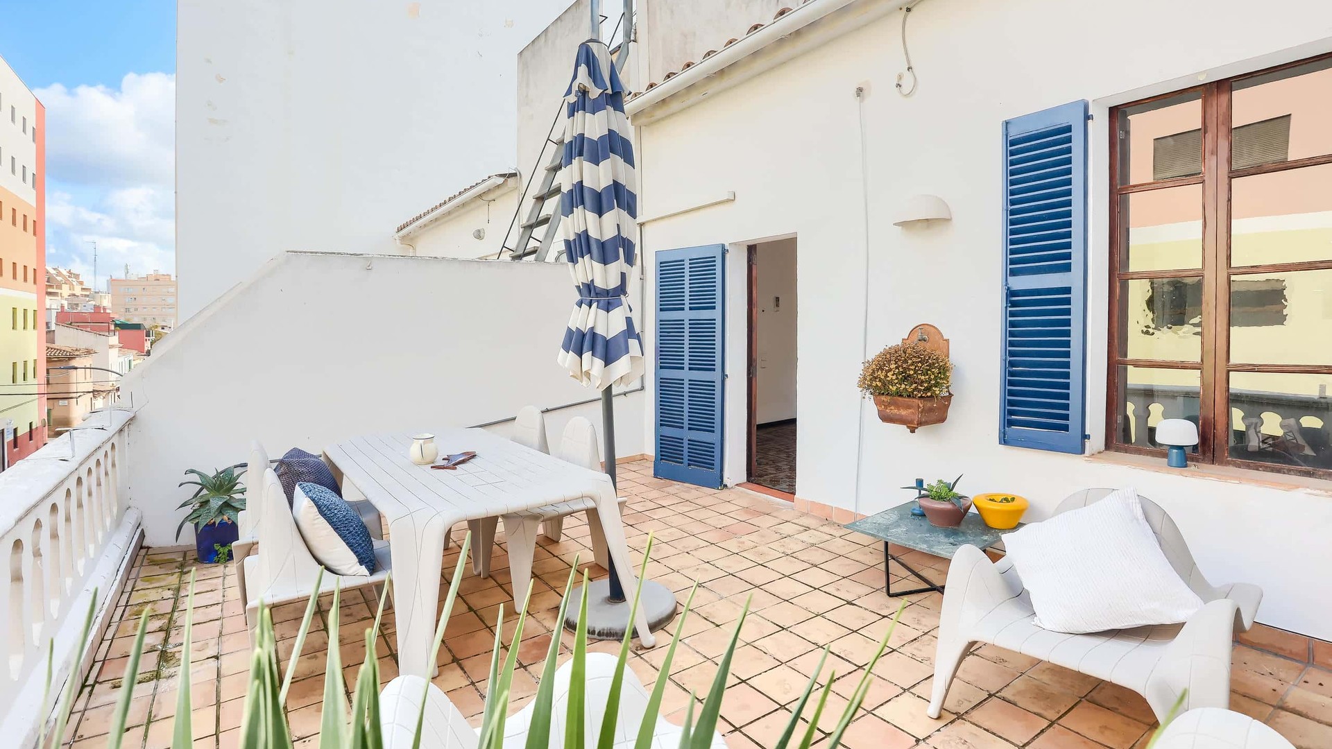 Outdoor terrace of a penthouse in Santa Catalina with white tiled flooring, blue shutter windows, and dining furniture.