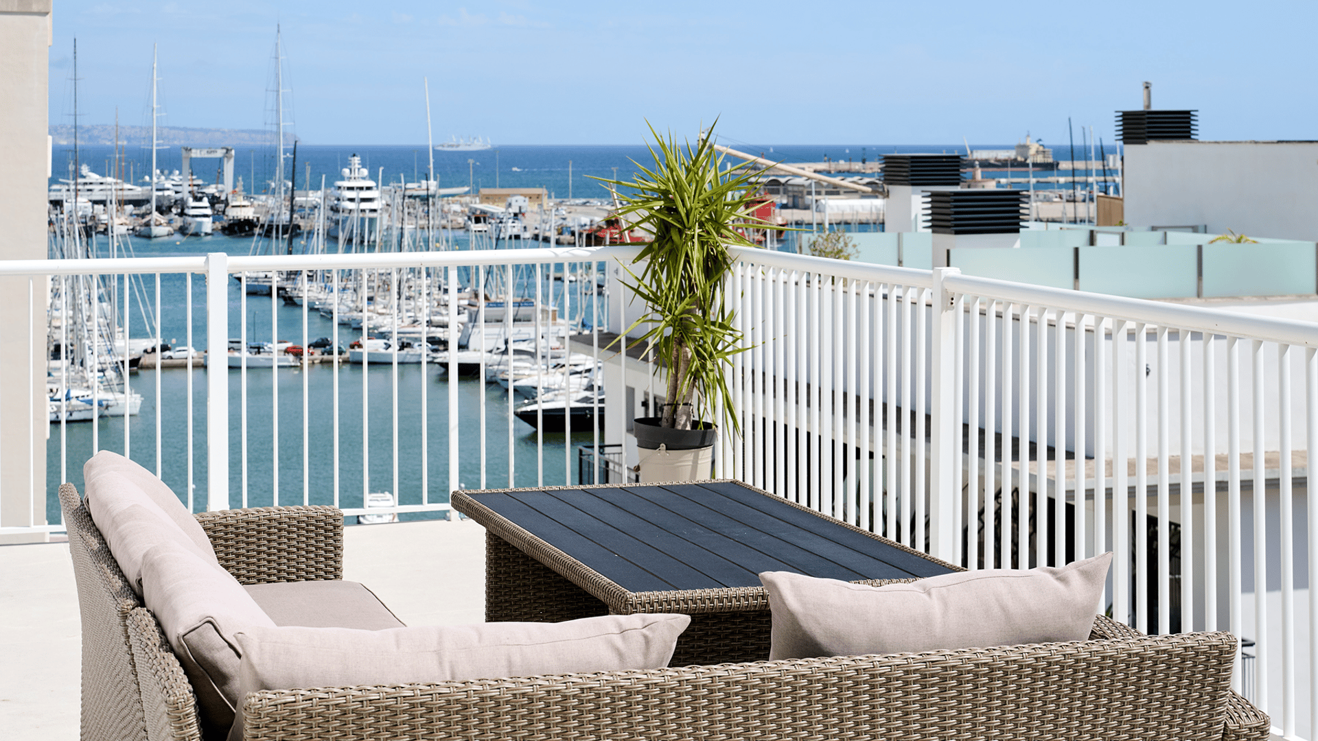 A rooftop terrace with wicker furniture overlooking a marina filled with boats under a clear blue sky in Santa Catalina.