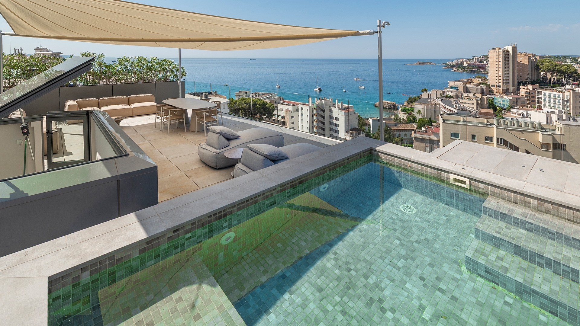 Elevated view of a penthouse terrace featuring a tiled plunge pool, outdoor dining area under a shade sail, and sea horizon.