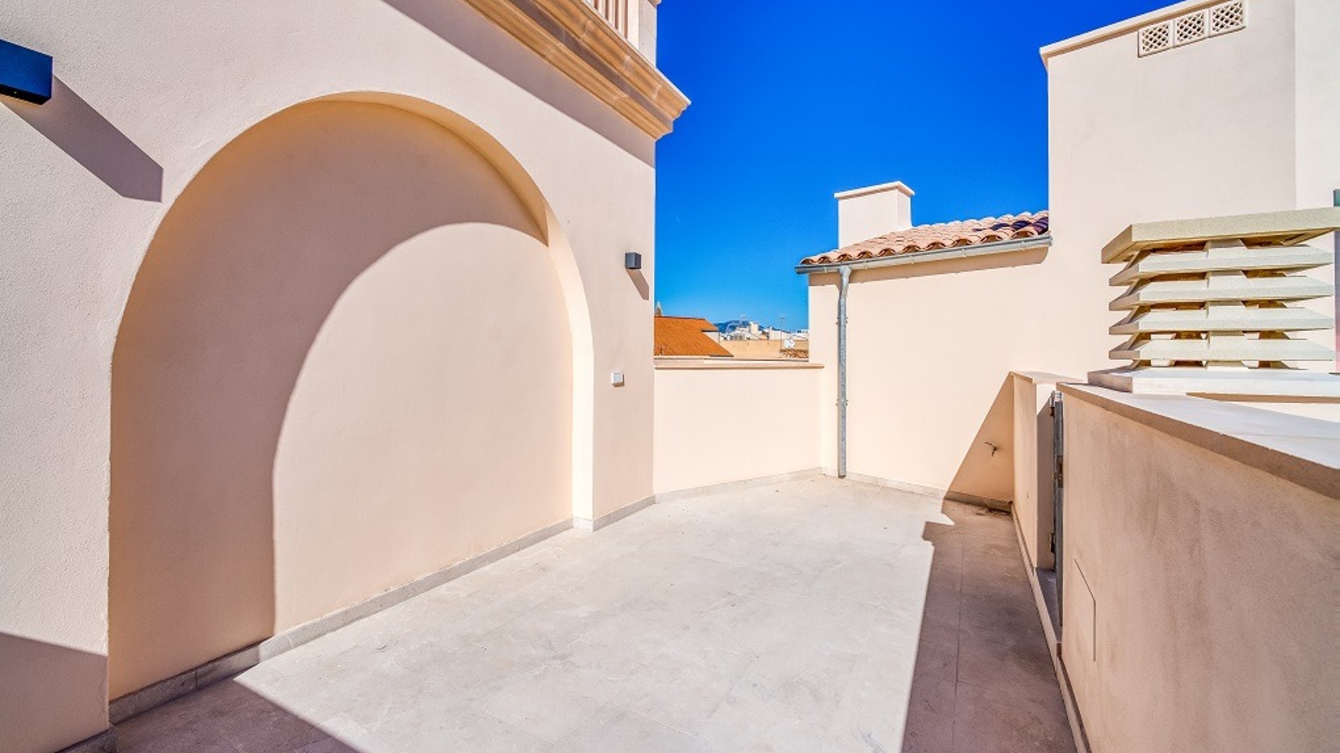 Empty rooftop terrace in Old Town with beige stucco walls, a large arched niche, and views toward traditional tiled rooftops.