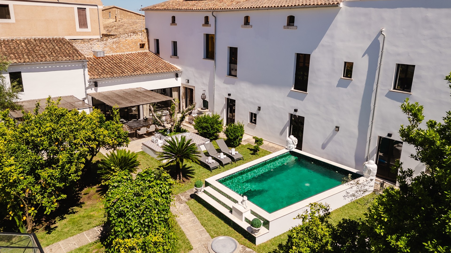 Aerial view of a white Mediterranean townhouse with a rectangular swimming pool, garden, and terracotta-tiled roof.