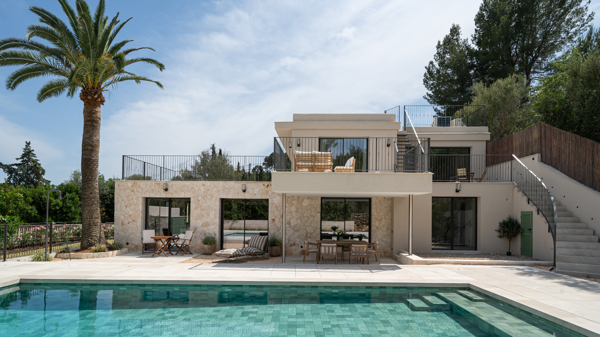 Facade of a two-story villa with pool in the foreground, exposed stone walls, and upper terrace.