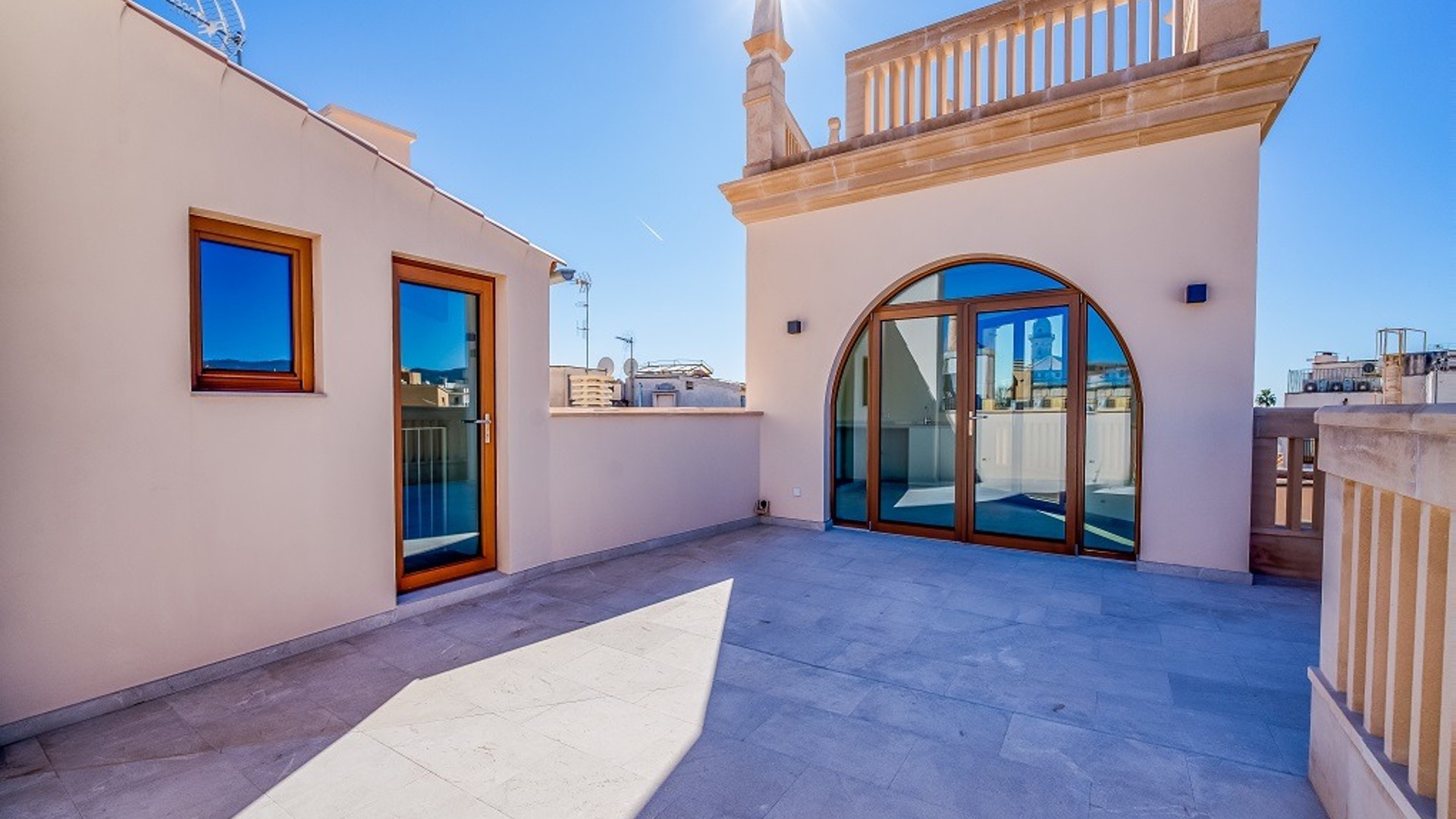 A sunny rooftop terrace with light-colored stone flooring, an arched glass door, and traditional architectural detailing.