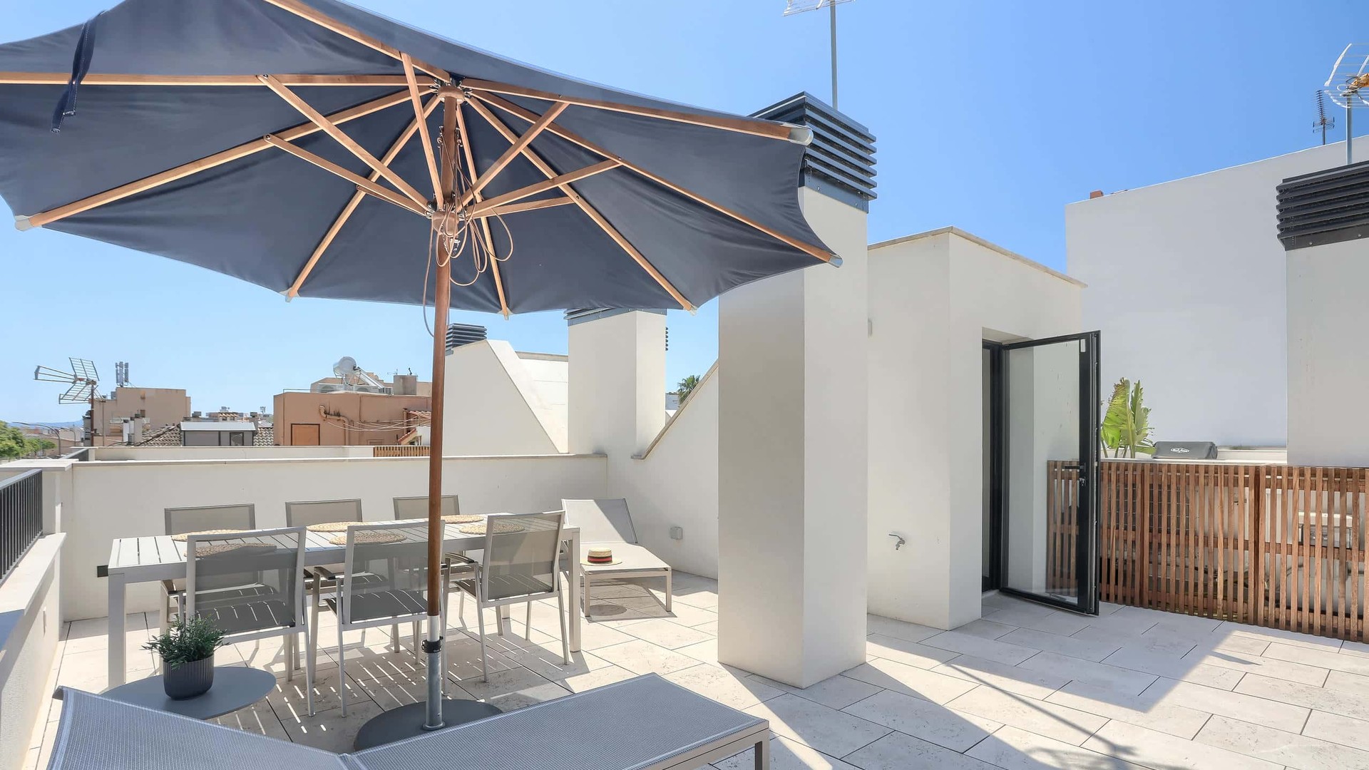 Rooftop terrace in El Molinar featuring a dining set under a grey parasol, sun loungers, and white stone flooring.
