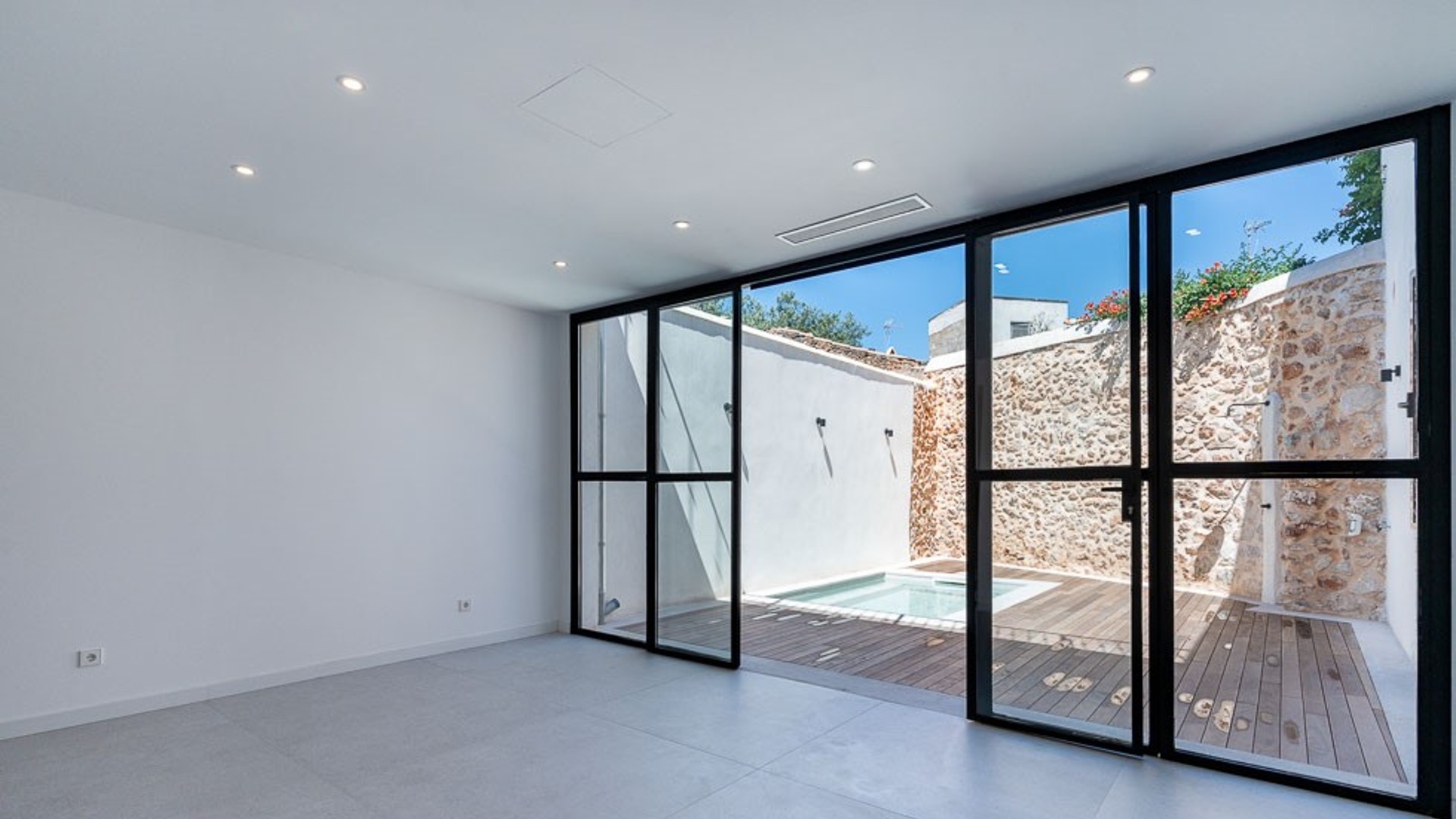 Modern interior living space featuring white walls, large black-framed glass sliding doors, and a view of a small pool.