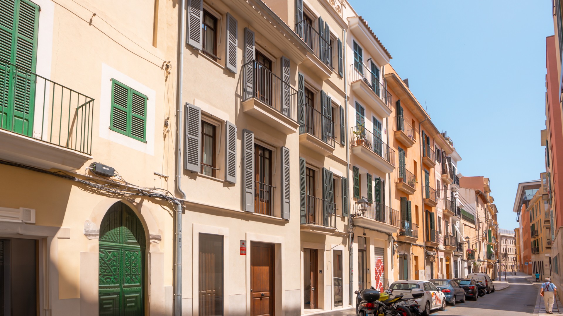 Multi-story Mediterranean townhouses featuring sand-colored plaster, green wooden shutters, and wrought-iron balconies.