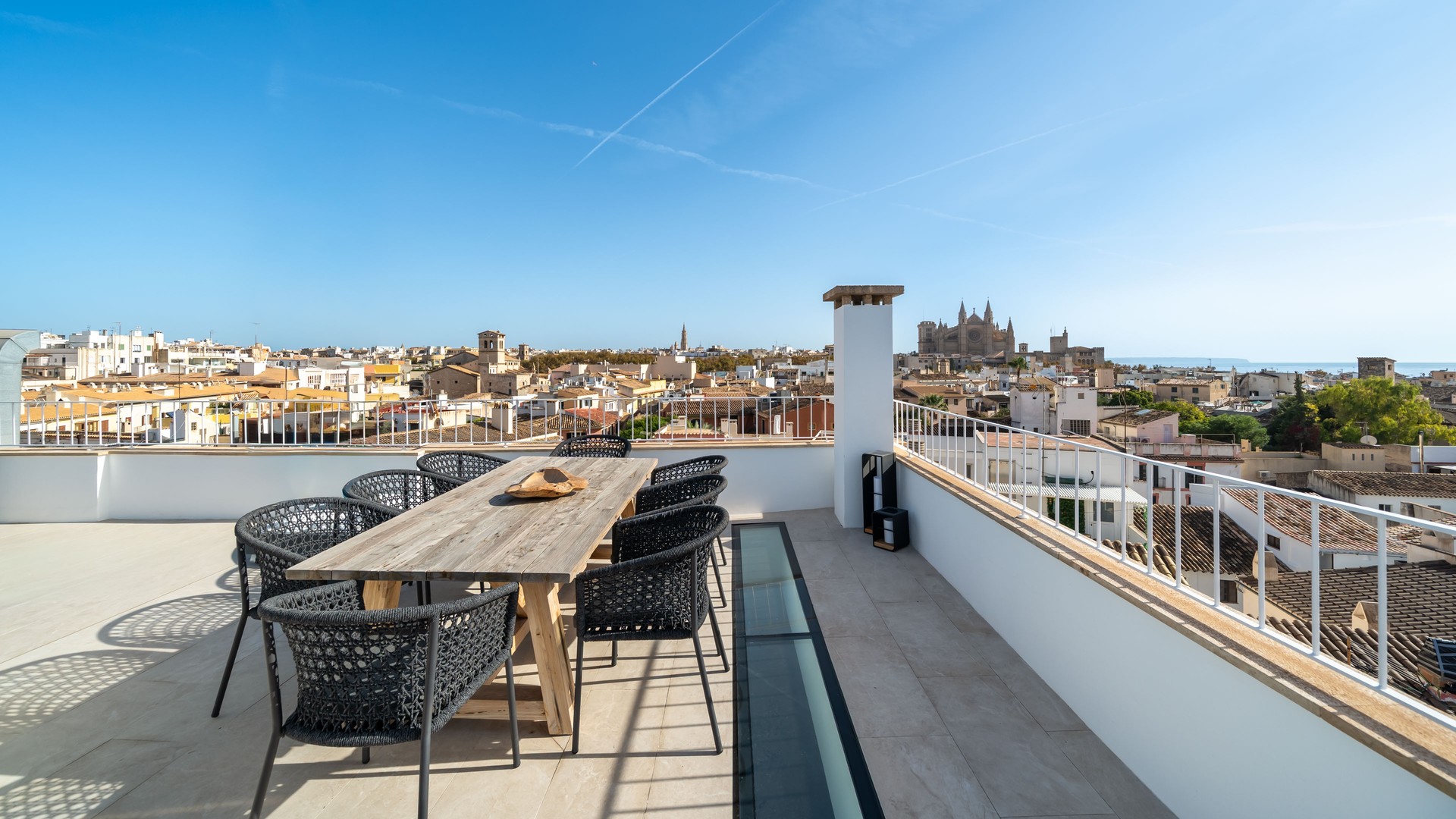 Expansive rooftop terrace with a wooden dining set overlooking the Palma city skyline and Cathedral under a clear blue sky.