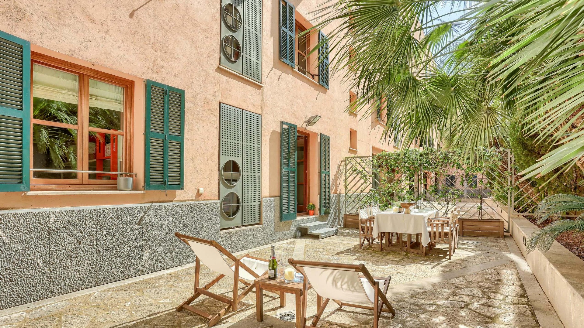 A private outdoor terrace in the Old Town featuring gravel flooring, white folding lounge chairs, a dining set, and pink stucco walls with green shutters.
