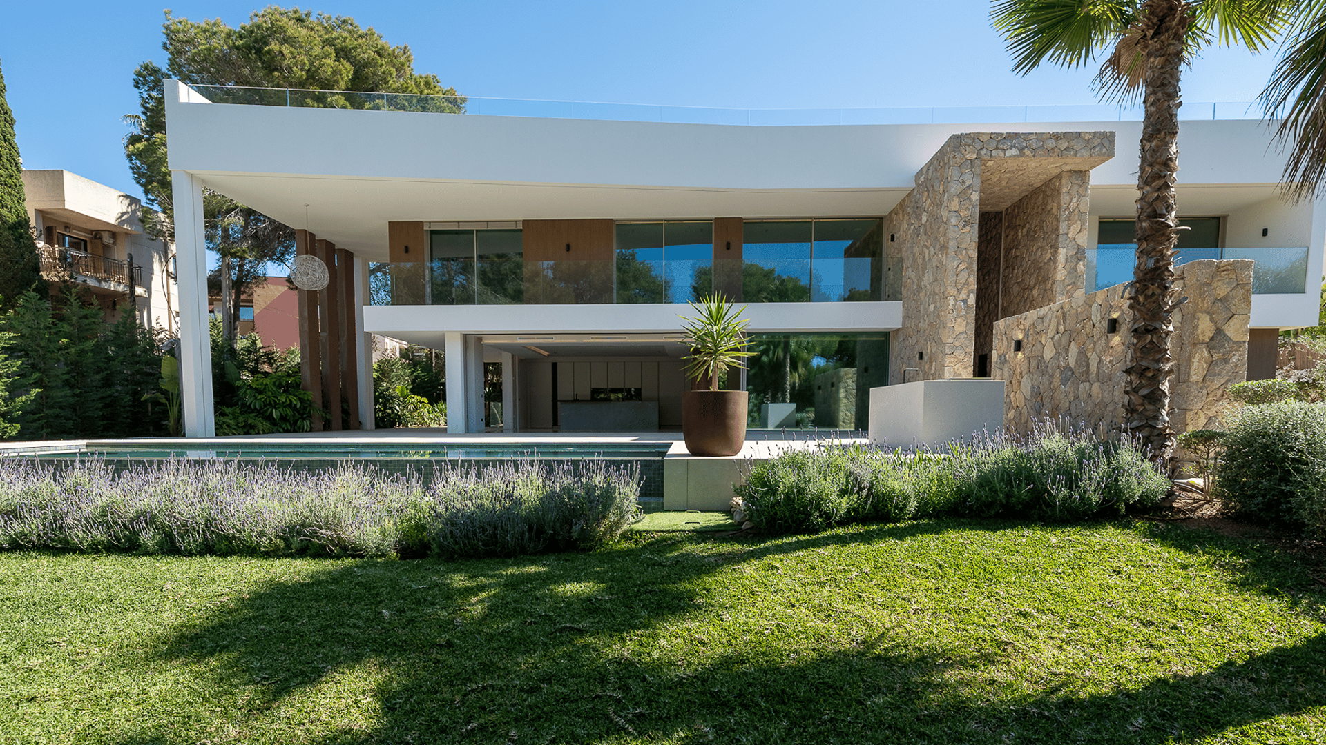Exterior view of a two-story modern villa in Santa Ponsa featuring white plaster, natural stone walls, and a swimming pool.