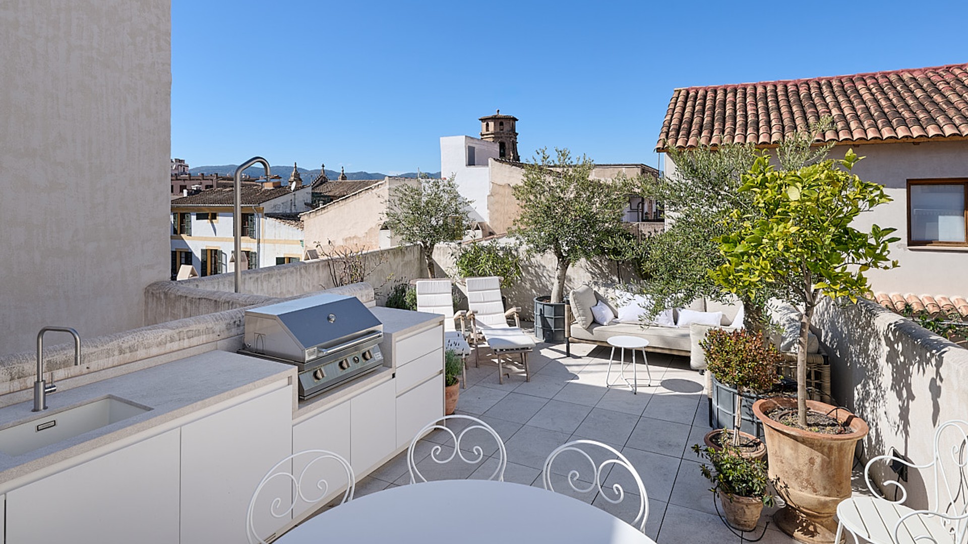 Sunny terrace featuring an outdoor kitchen, barbecue, lounge area, and views of the Old Town rooftops.
