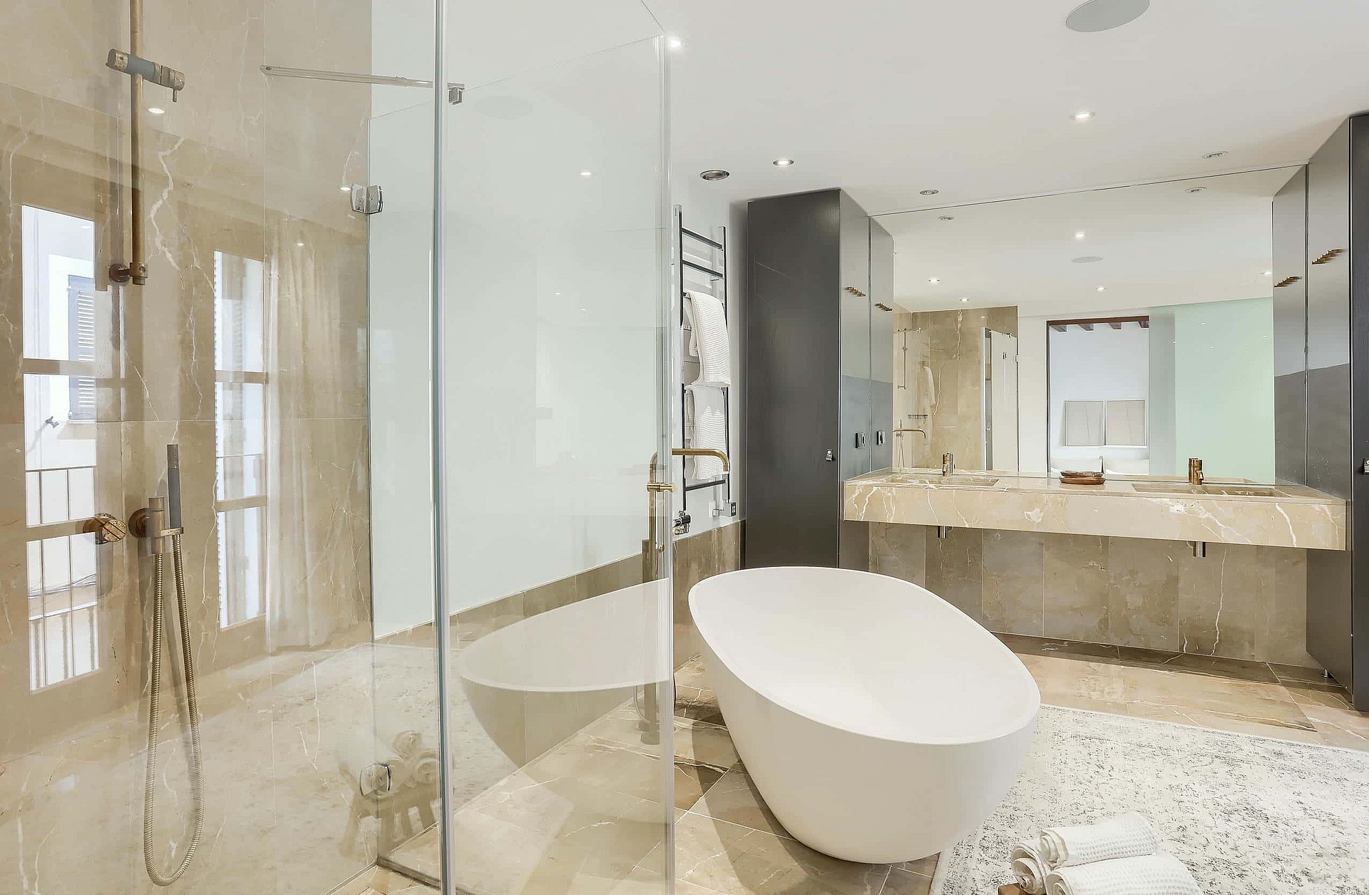 Modern bathroom featuring a white freestanding bathtub, glass-enclosed shower, and long stone vanity with double sinks.