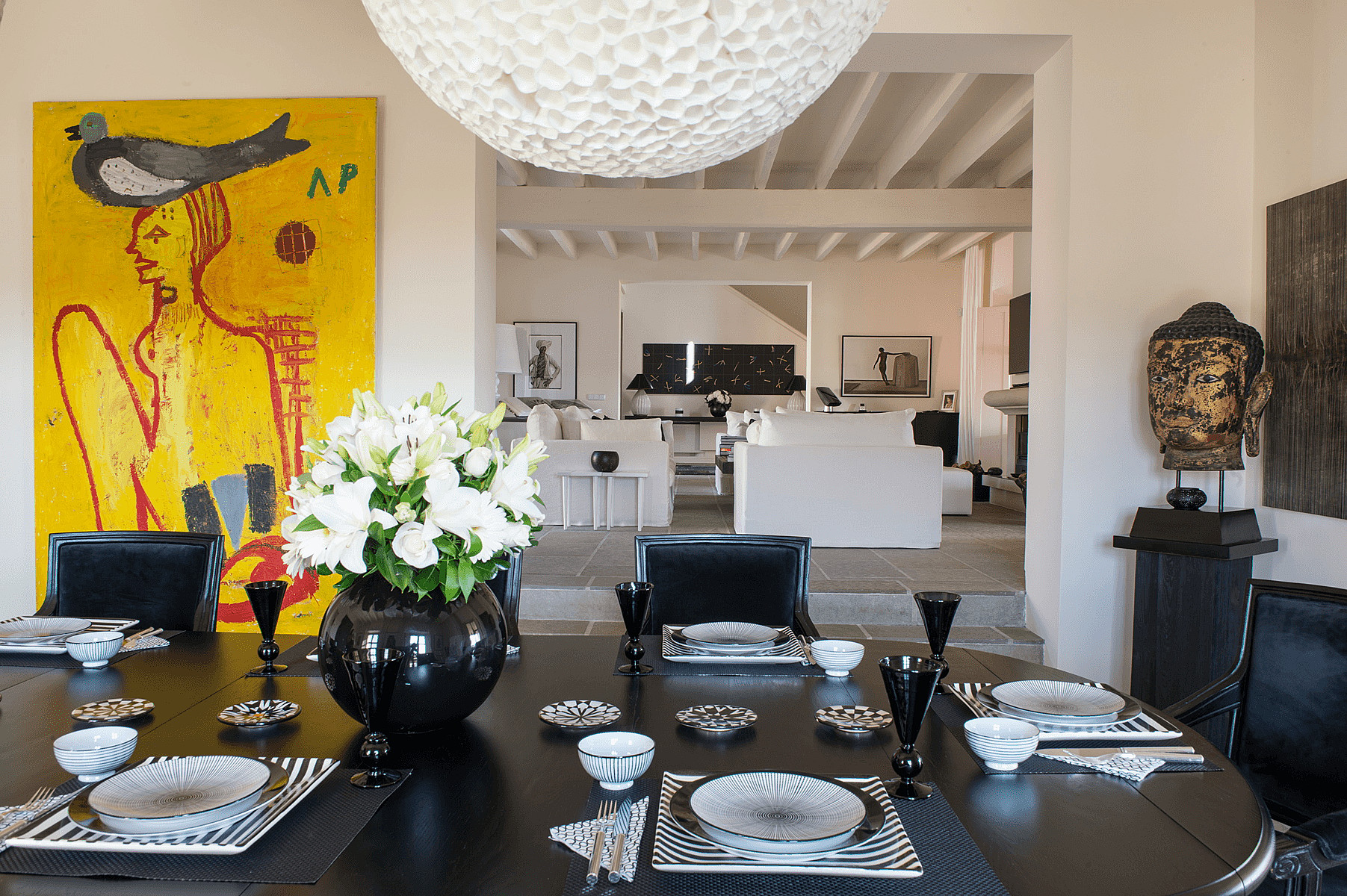 Dining room featuring a round black table, black leather chairs, and a large yellow painting on the wall.