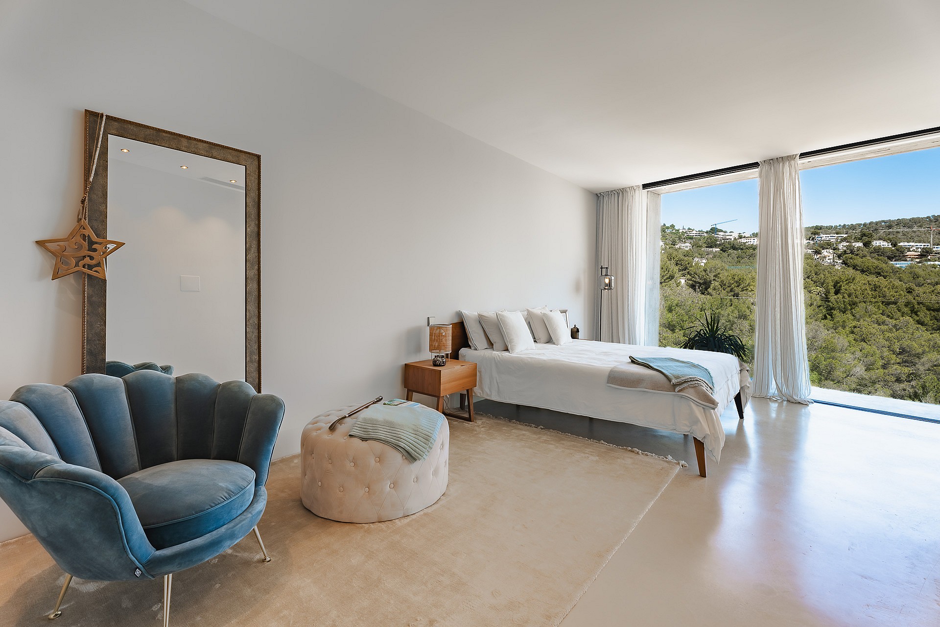 Minimalist bedroom featuring floor-to-ceiling windows, mountain views, a blue velvet chair, and polished stone floors.
