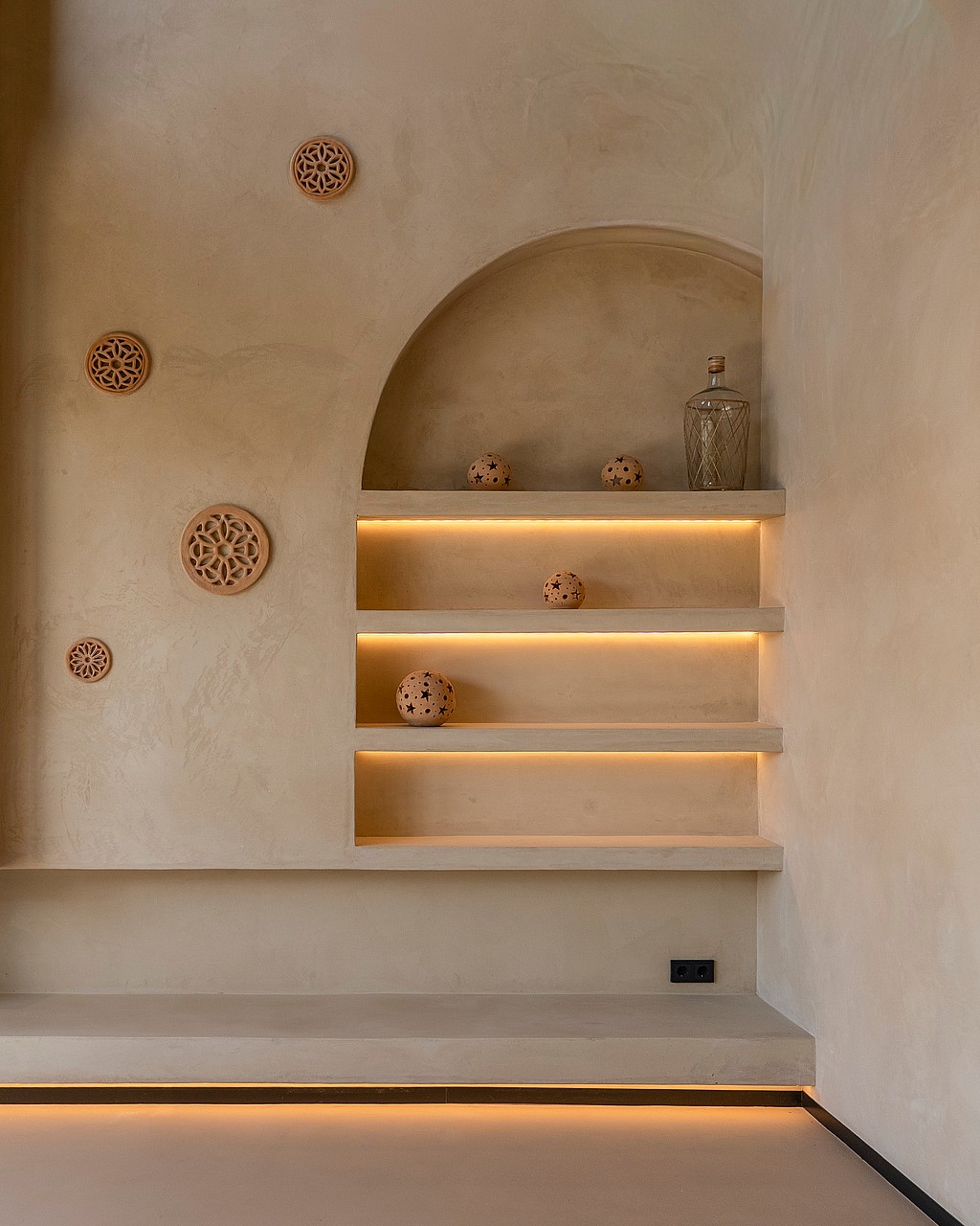 A beige textured wall featuring a recessed arched shelf system with warm LED strip lighting and decorative terracotta objects.