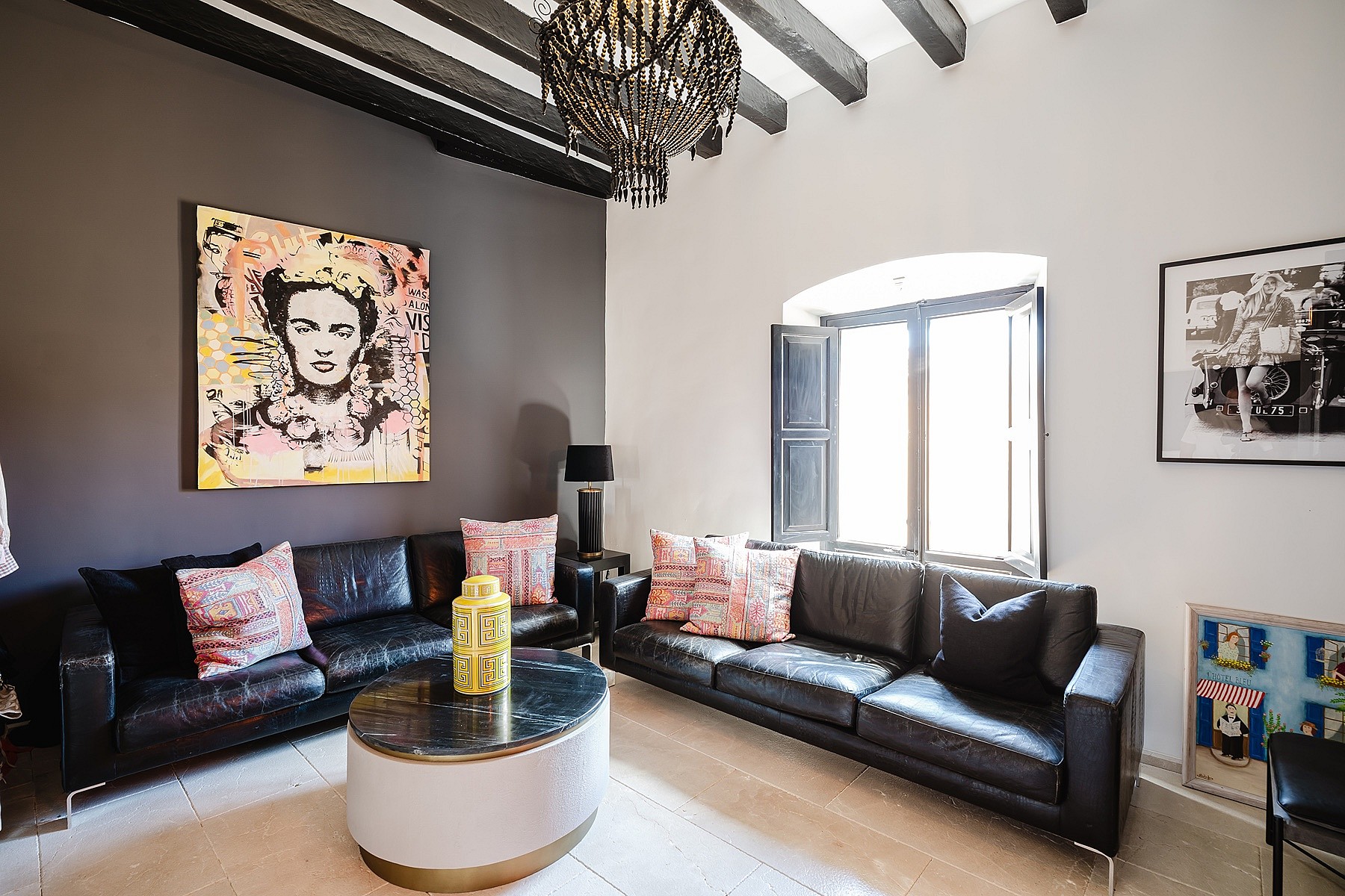 A living room with two black leather sofas facing a central coffee table, dark gray accent wall, and exposed dark ceiling beams.