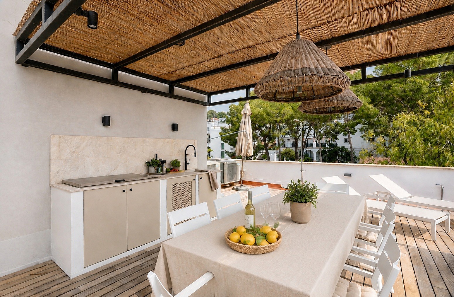Outdoor dining terrace featuring a wicker-covered pergola, a built-in stone kitchen station, and a long dining table.
