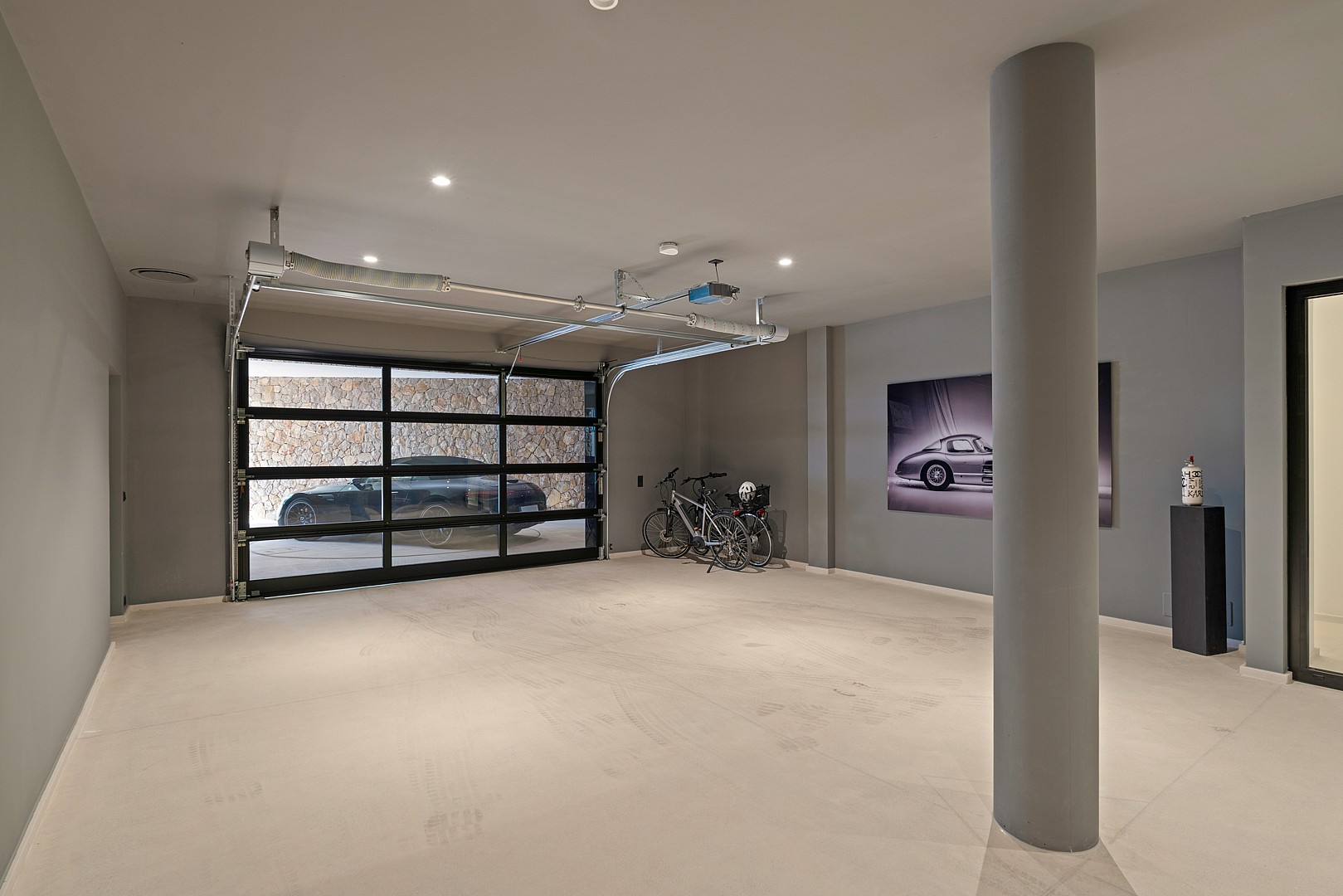 Interior view of a modern underground garage with light grey walls, concrete floors, and a metal and glass sectional door.