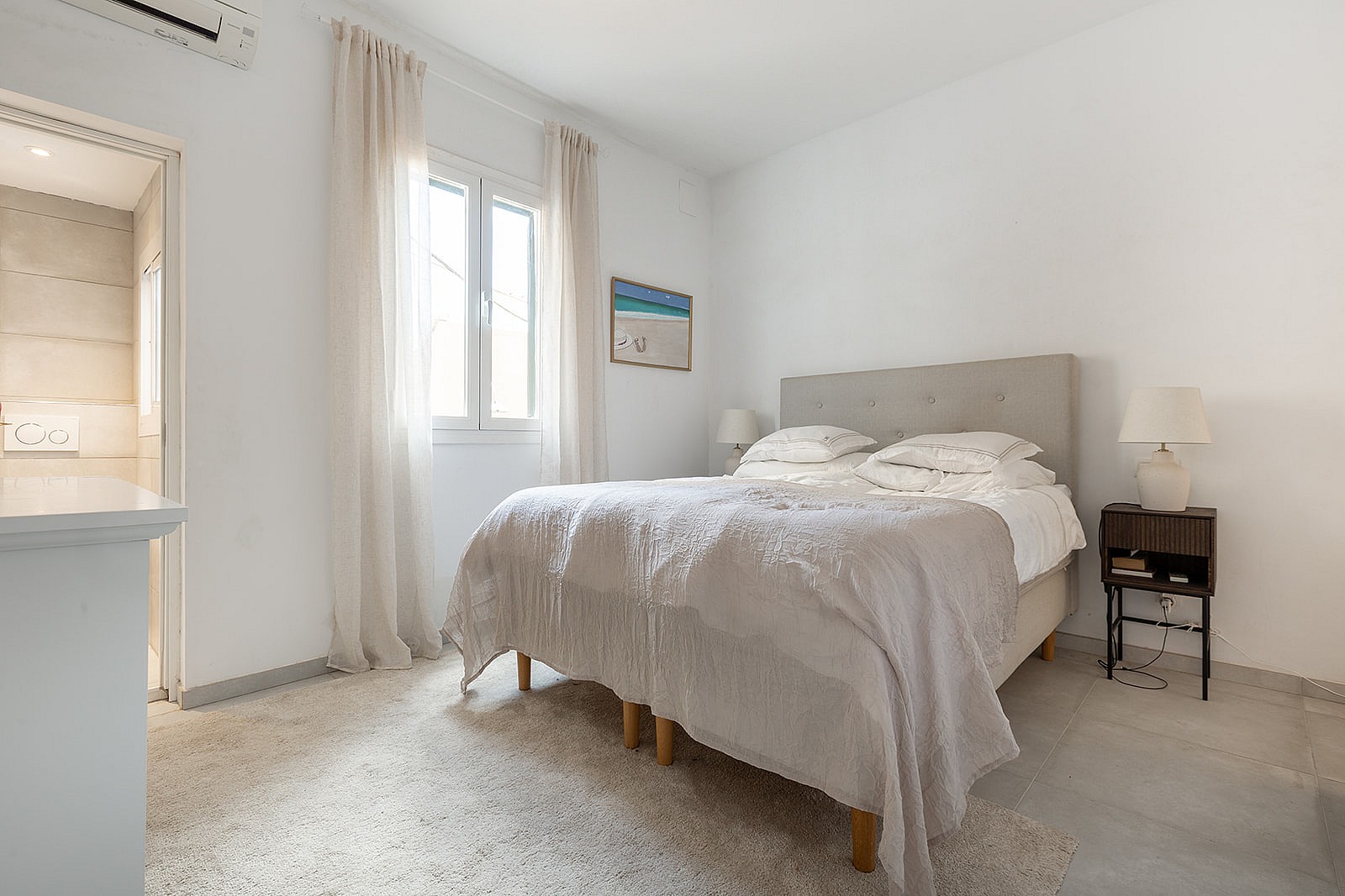 A minimalist bedroom featuring a double bed, beige curtains, soft area rug, and a small dark wood nightstand.