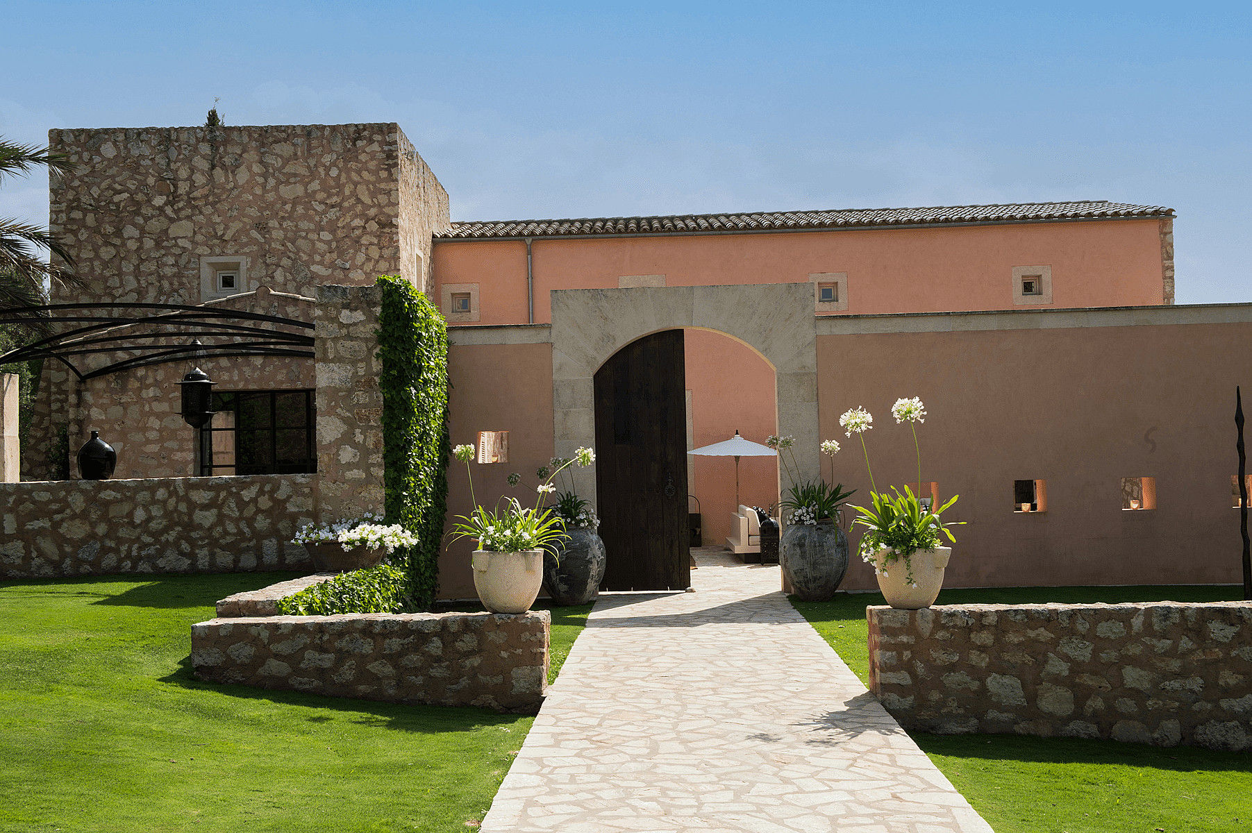 A stone paved path leads through an arched wooden gate into a courtyard of a traditional Finca in Algaida.