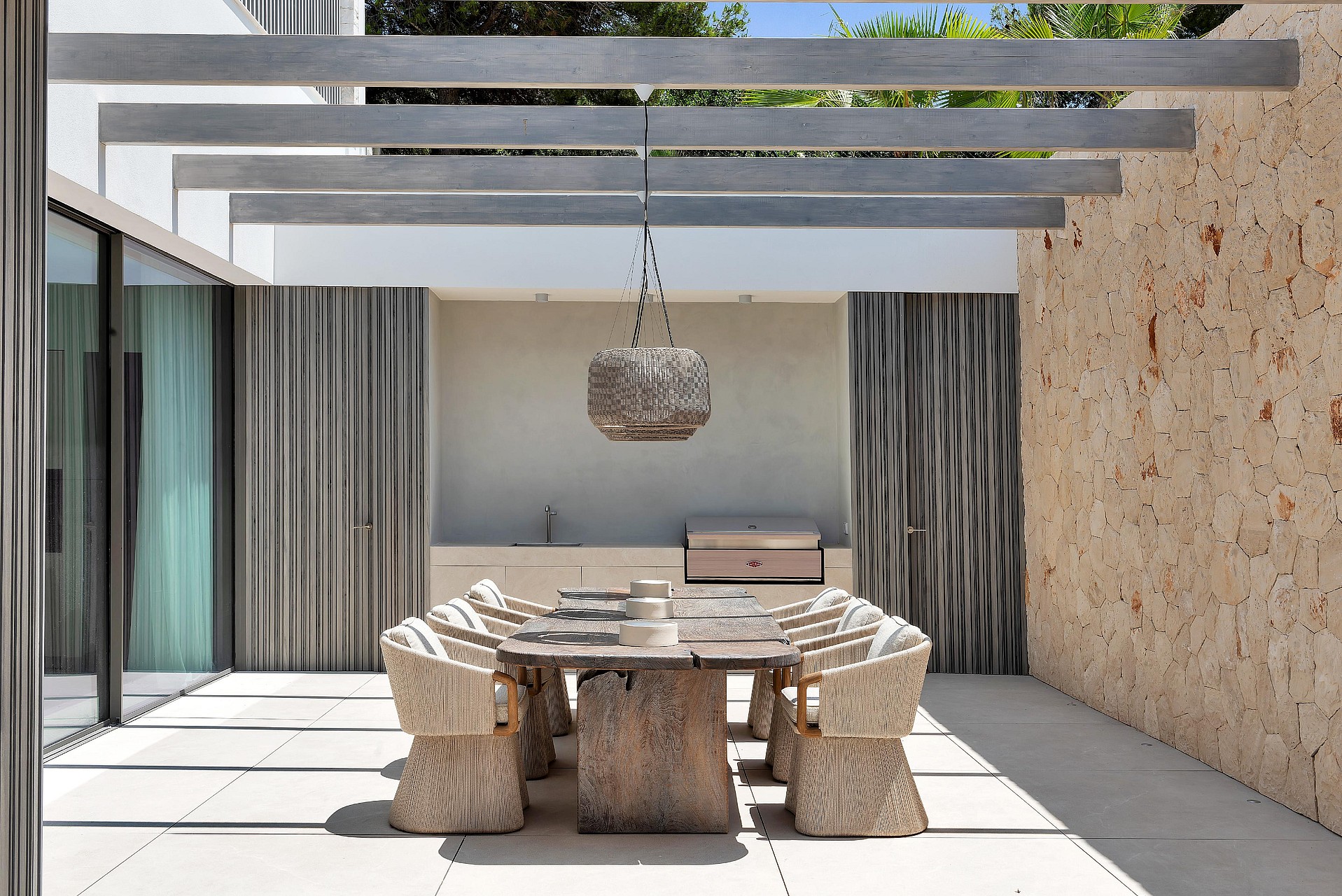 Covered outdoor dining area with exposed beam pergola, Mallorcan stone wall and wicker pendant lights