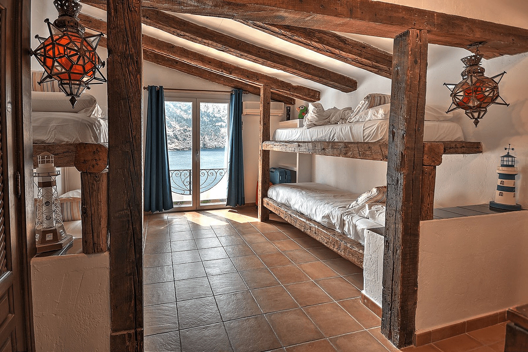 Bunk bedroom featuring exposed wood ceiling beams, tiled flooring, and brass pendant lanterns, with a view of the sea.