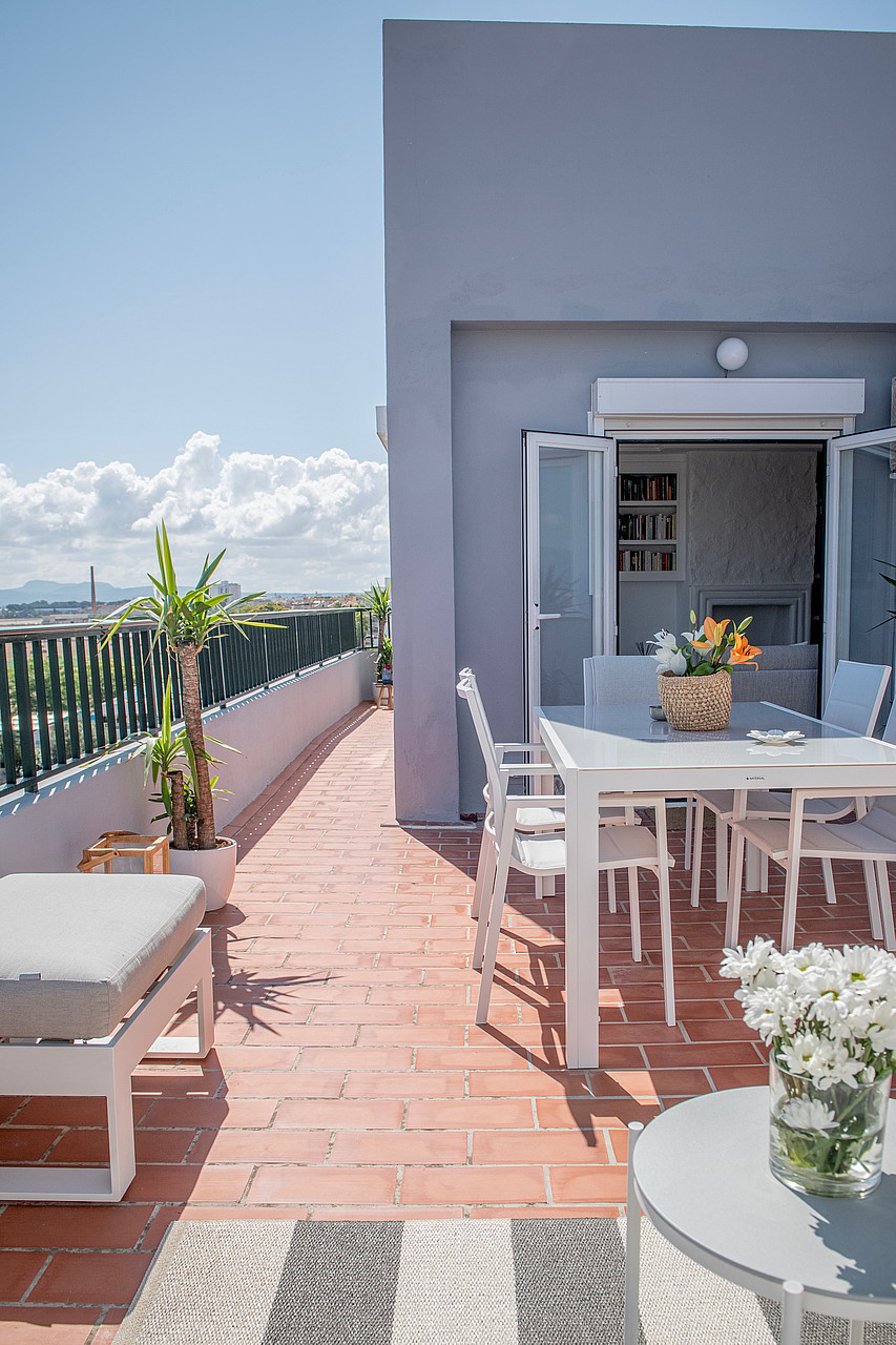 A sunlit rooftop terrace in El Molinar with a white dining set, terracotta tiles, and mountain views in the background.
