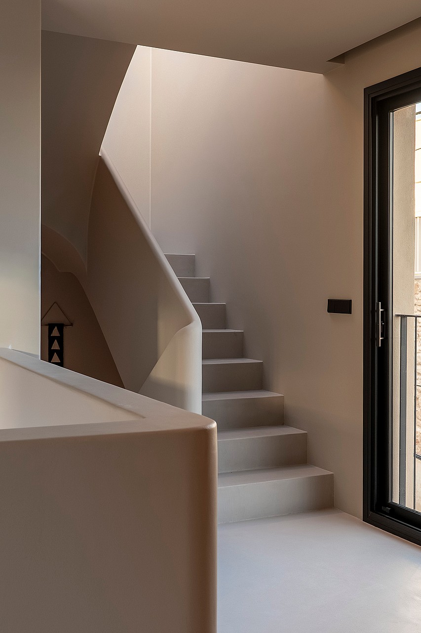 Modern staircase with seamless microcement finish, sculptural handrail, and black-framed door in a Genova townhouse.
