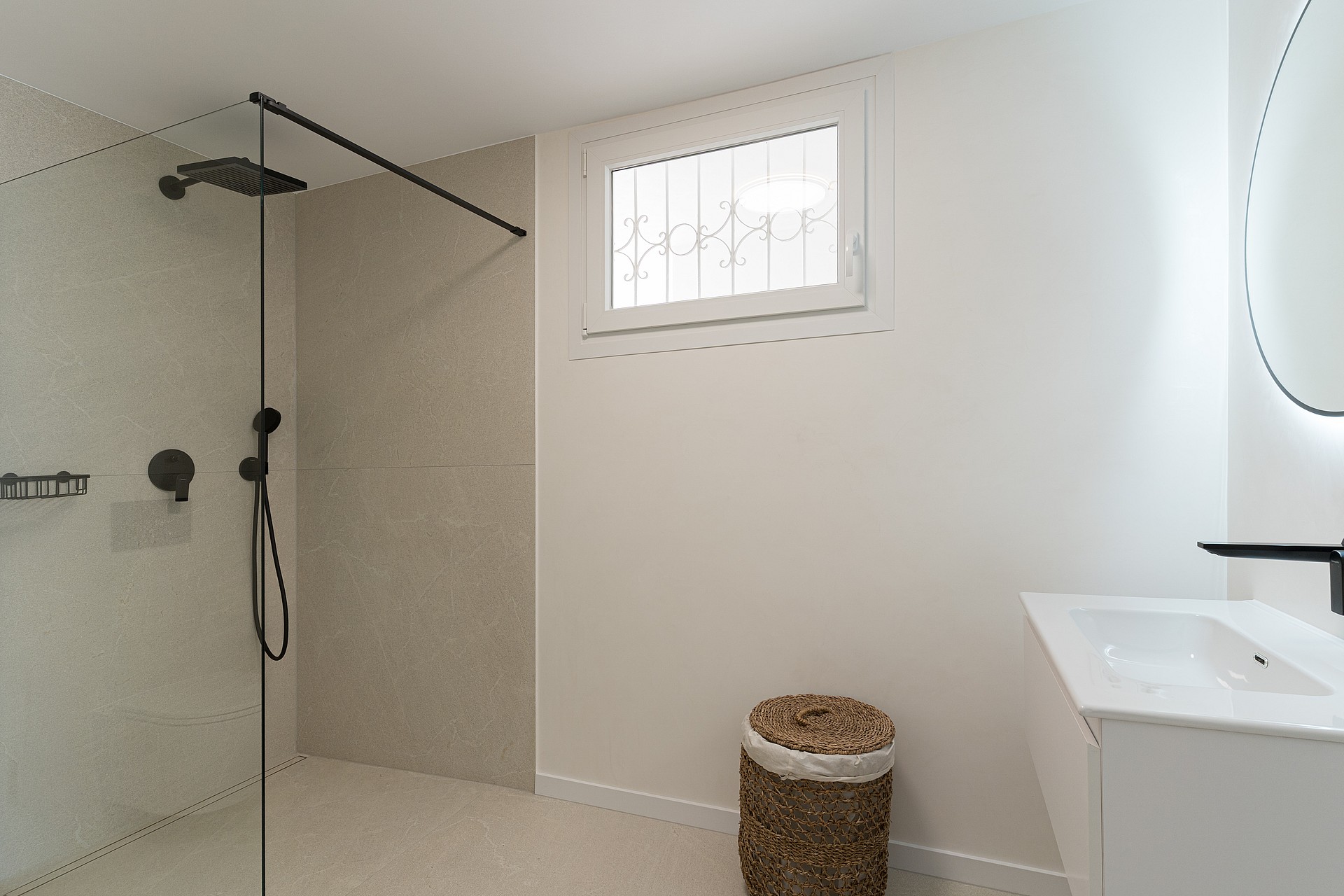 A contemporary walk-in shower featuring a glass partition, matte black rain shower head, and large-format sand-colored tiles.