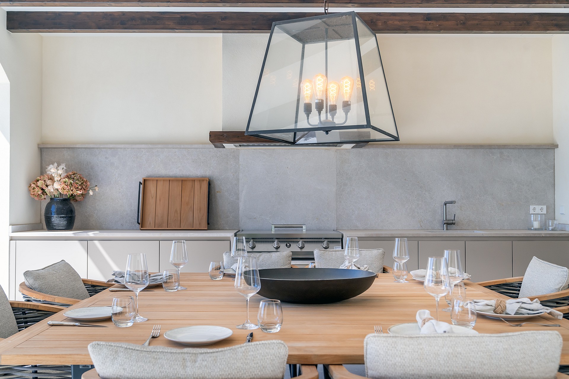 A solid oak dining table sits beneath dark wood ceiling beams and a large glass lantern pendant in a bright interior.