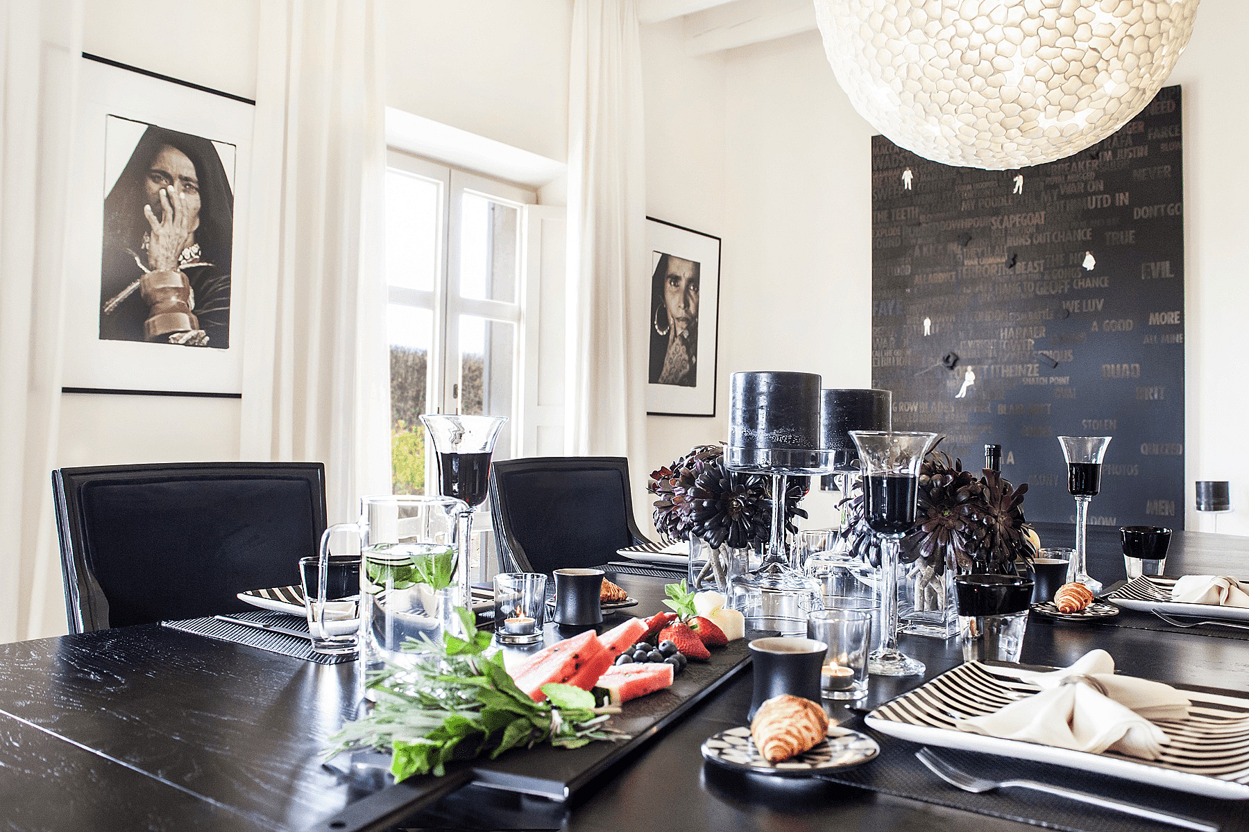 A formal dining room interior with a black lacquered table, black dining chairs, a large textured spherical pendant light, and framed monochrome photography on white walls.