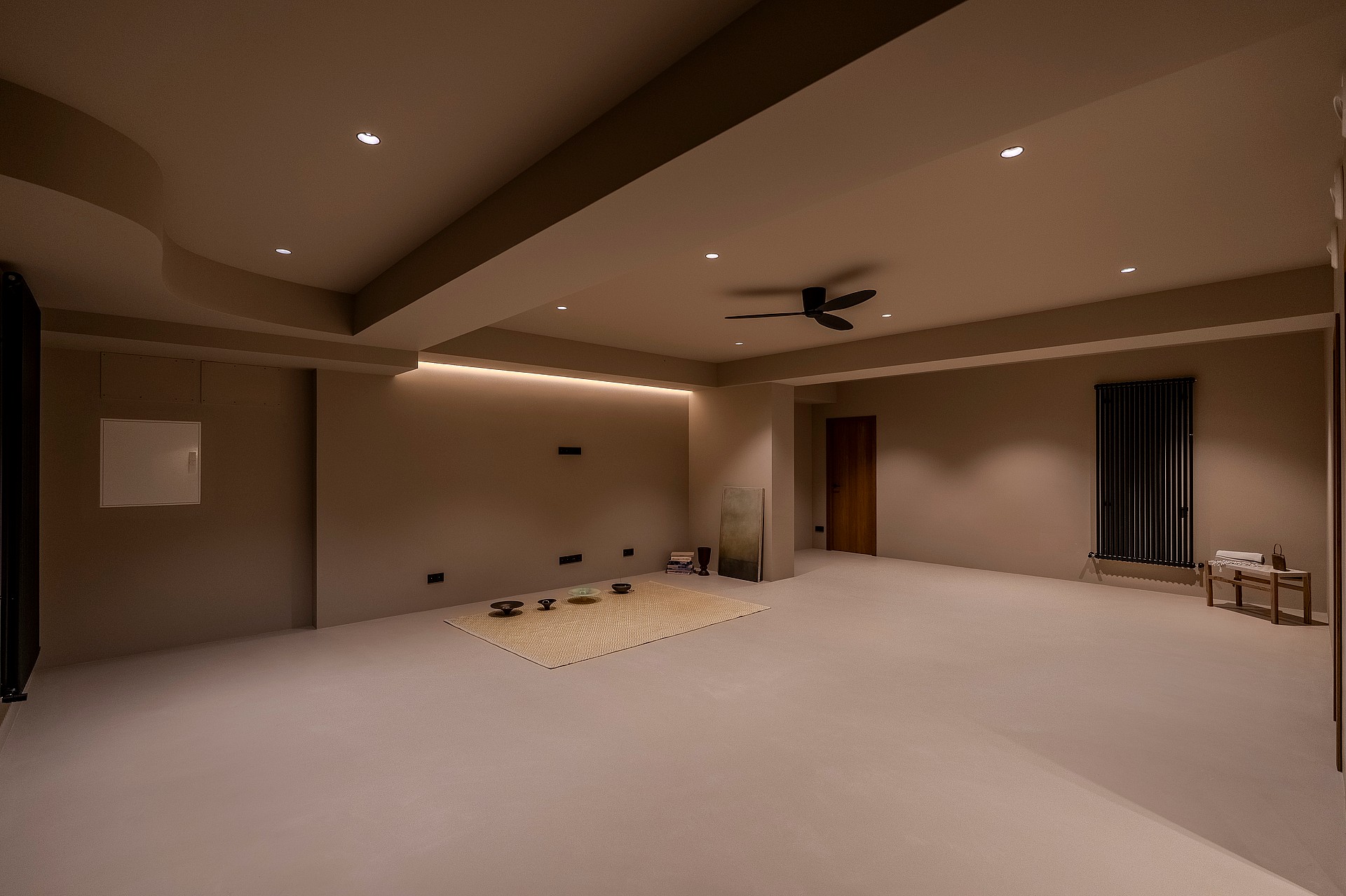 A large empty interior room with taupe walls, warm recessed spotlighting, a dark ceiling fan, and integrated LED strips.