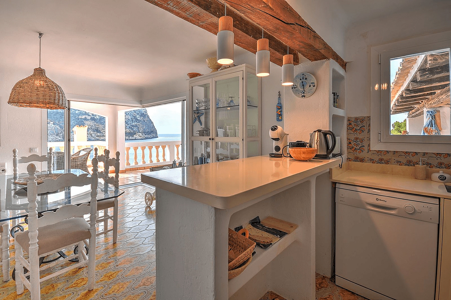 Kitchen and dining area with white cabinets, patterned tiled floor, and views of the Mediterranean coastline.