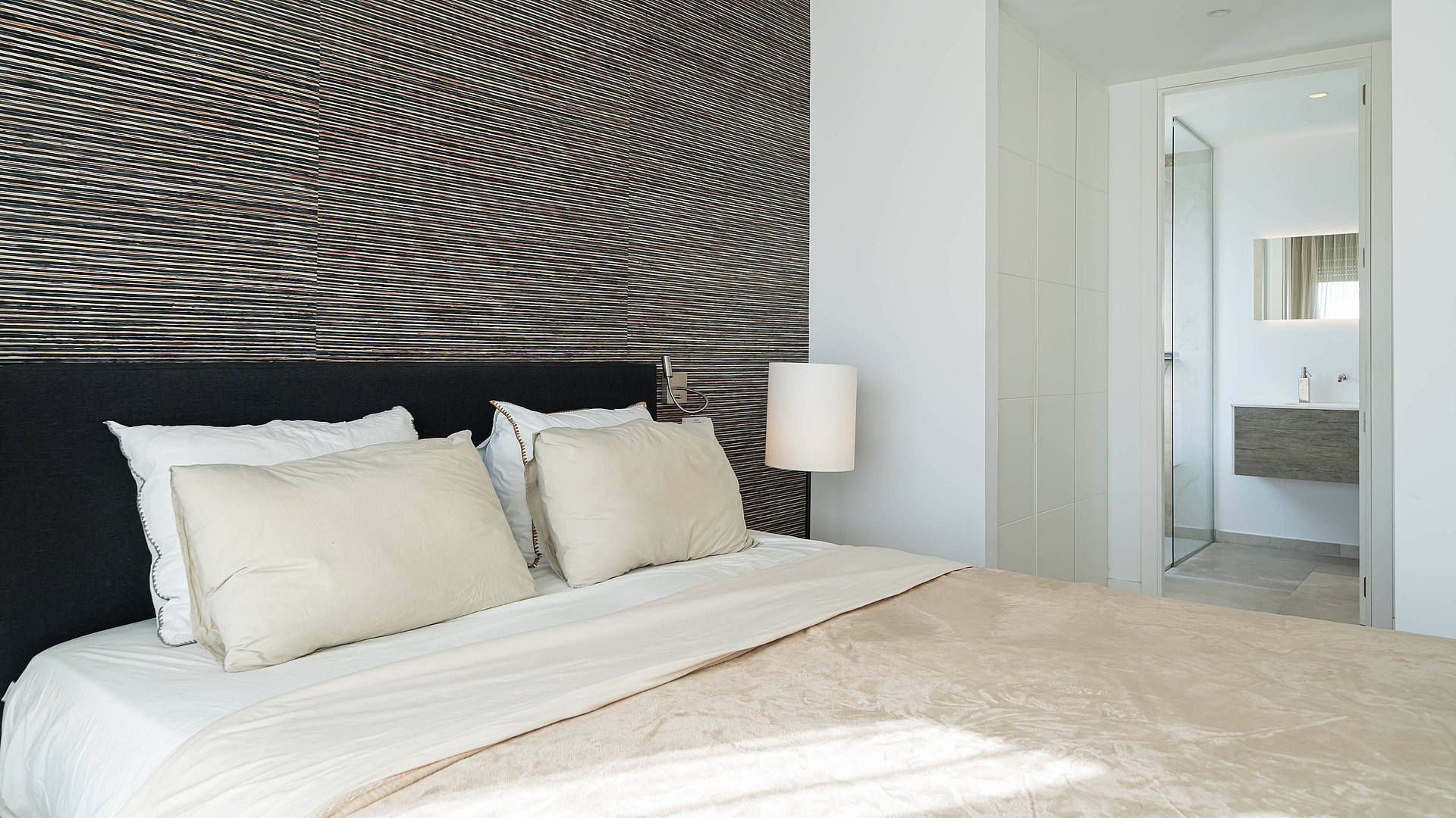 Close-up of a king-size bed featuring a dark upholstered headboard and a wall panel with horizontal ridged texture.