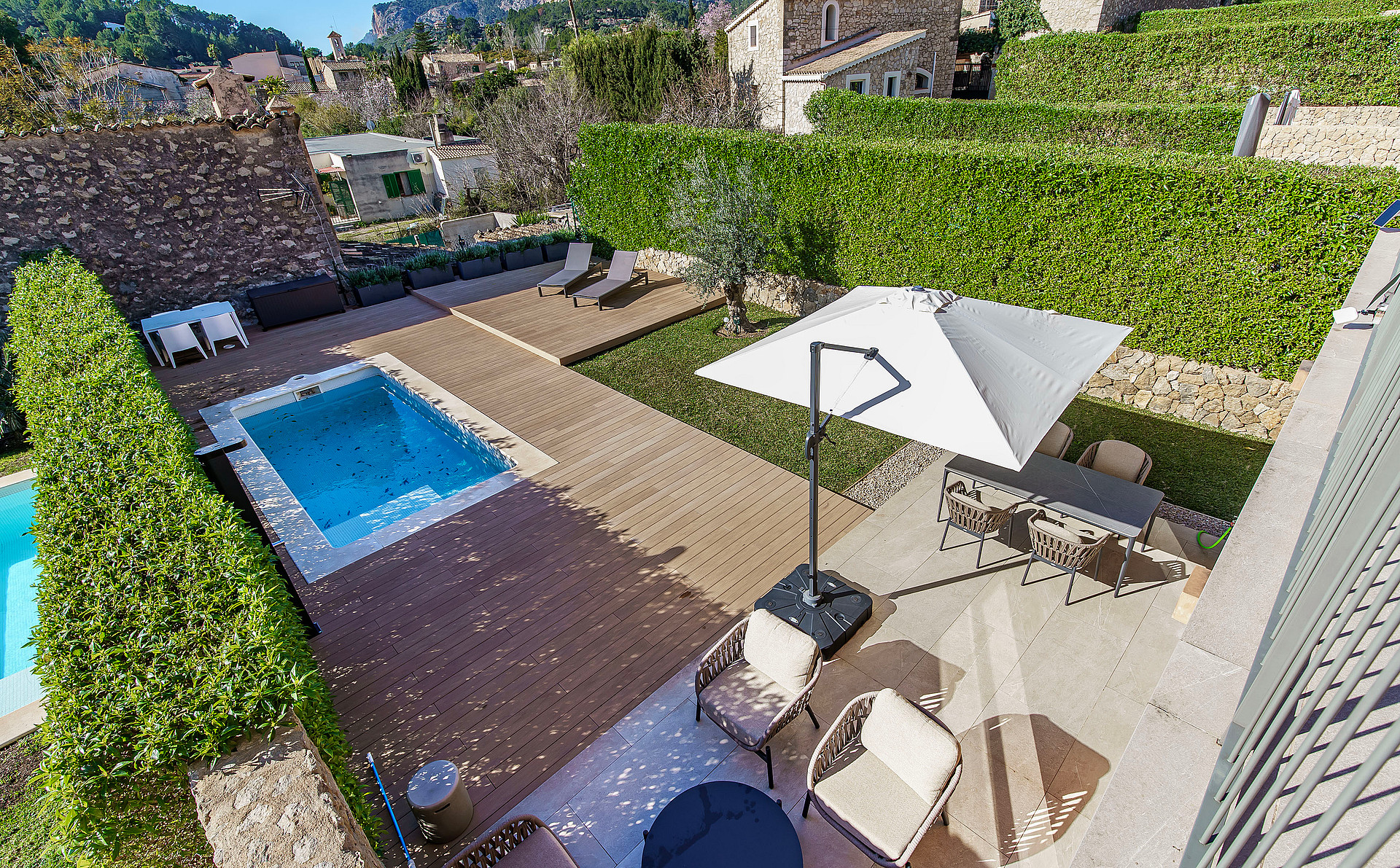 Aerial view of a private backyard featuring a swimming pool, sun loungers, dining area with a parasol, and stone walls.